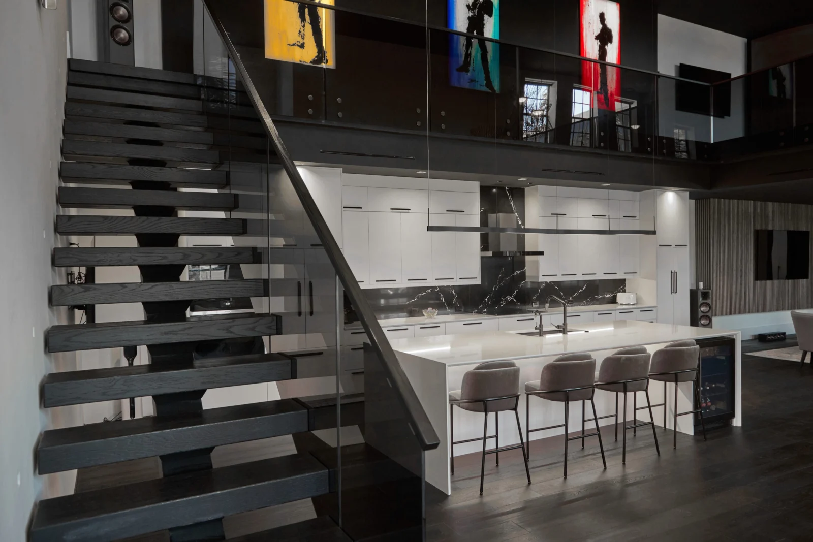 Black floating stair with tinted gray glass panels silhouetted against a white kitchen and island seating