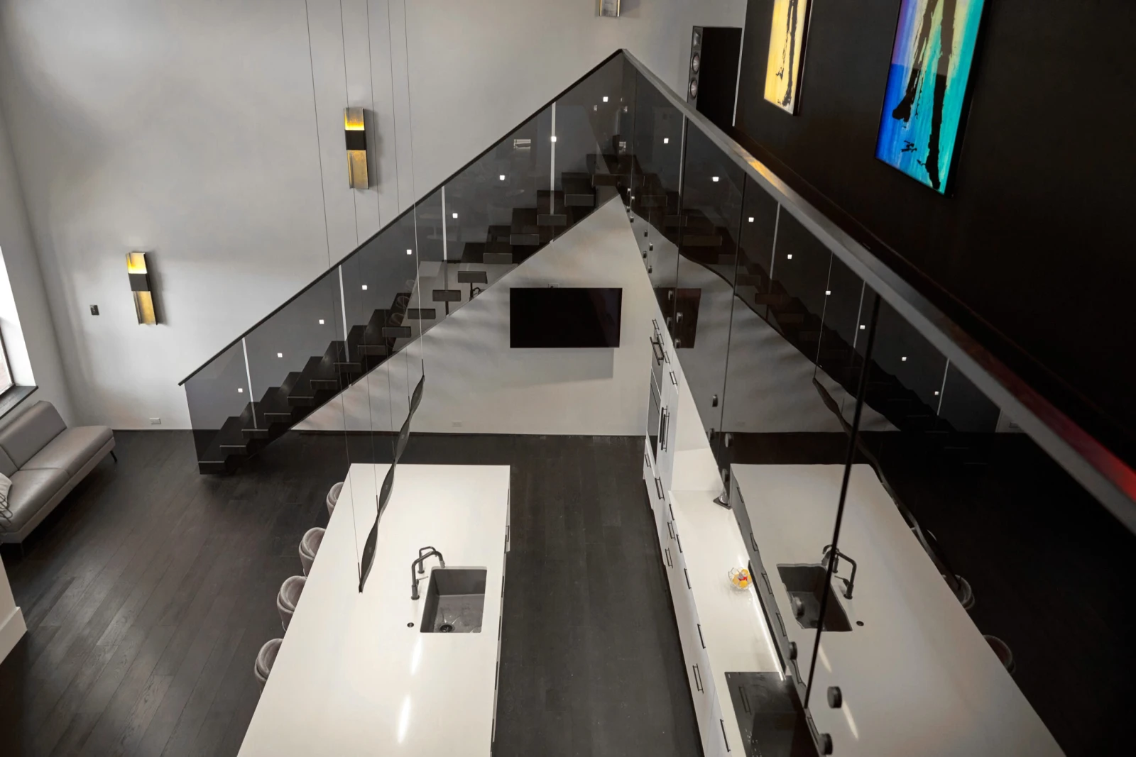Looking down from the balcony onto white kitchen islands past tinted glass railing