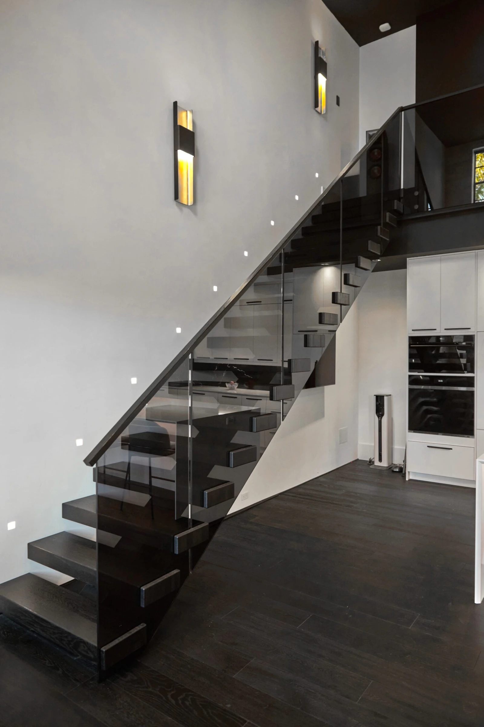 Stair climbing to the upper level with glass railing beside white cabinetry