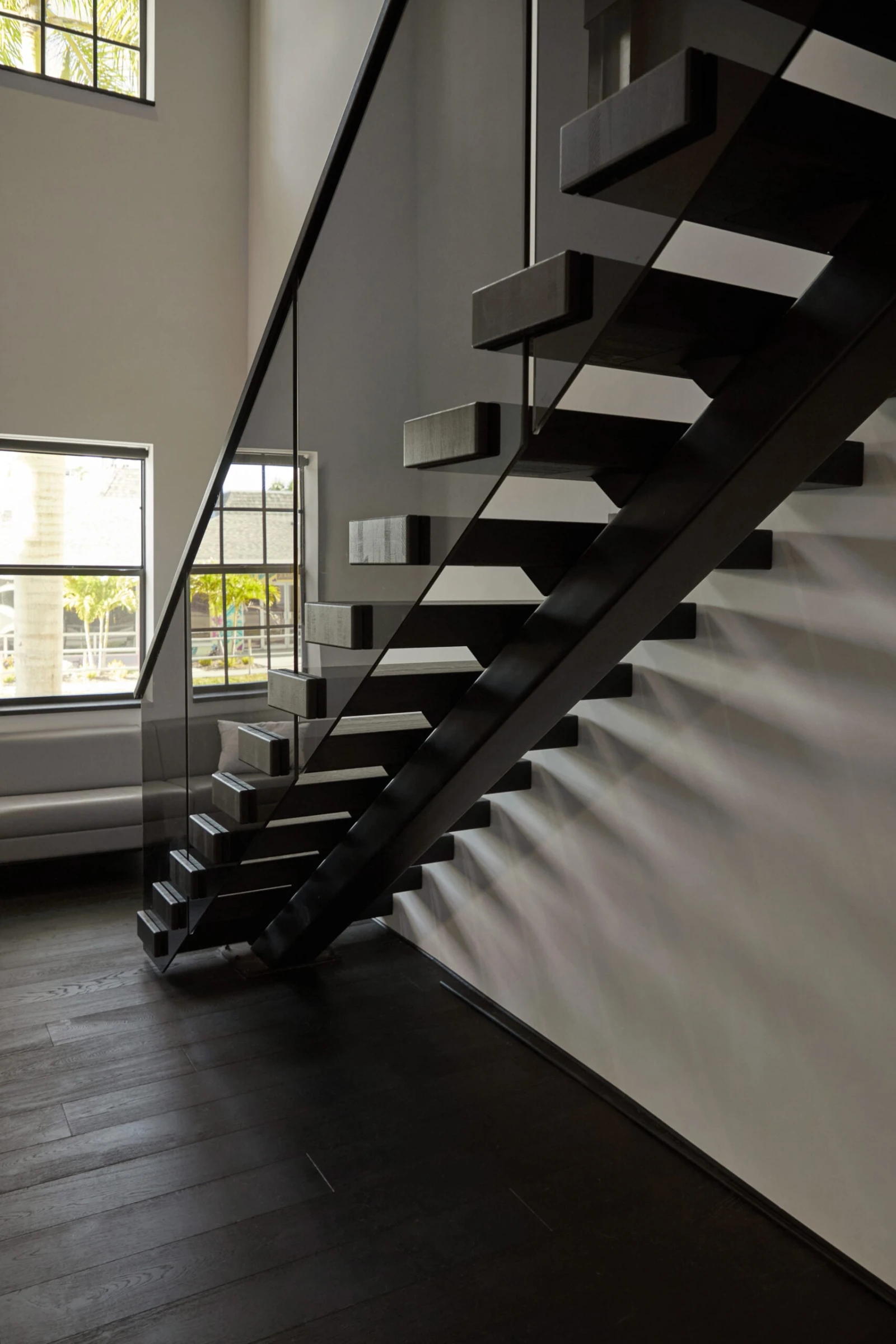 Floating treads against a white wall with windows and dark flooring below