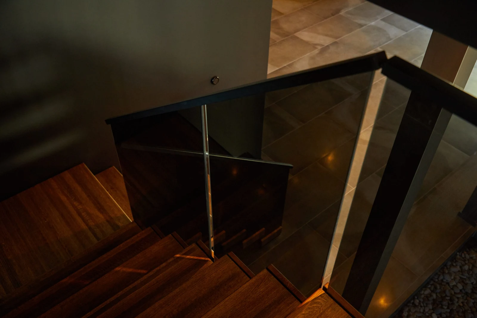 Dim overhead view of treads and the glass railing corner with tile beyond