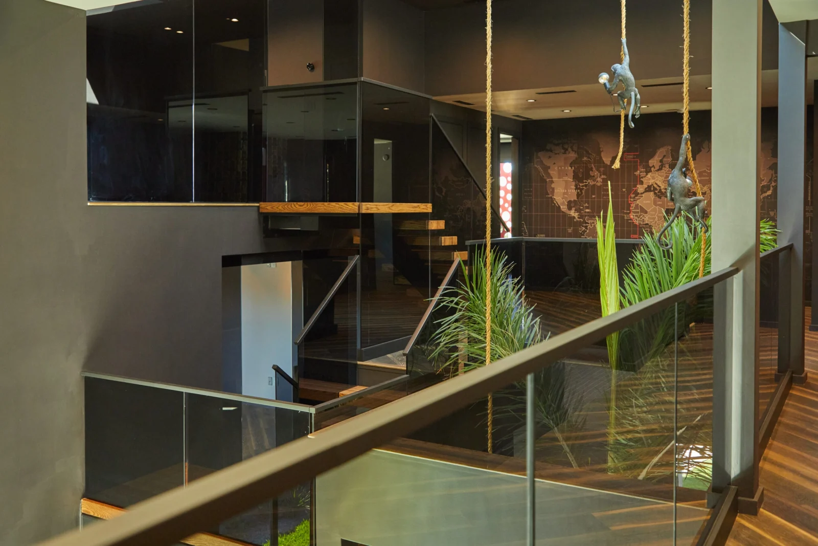 Looking across the upper glass railing toward hanging sculptures and a map wall