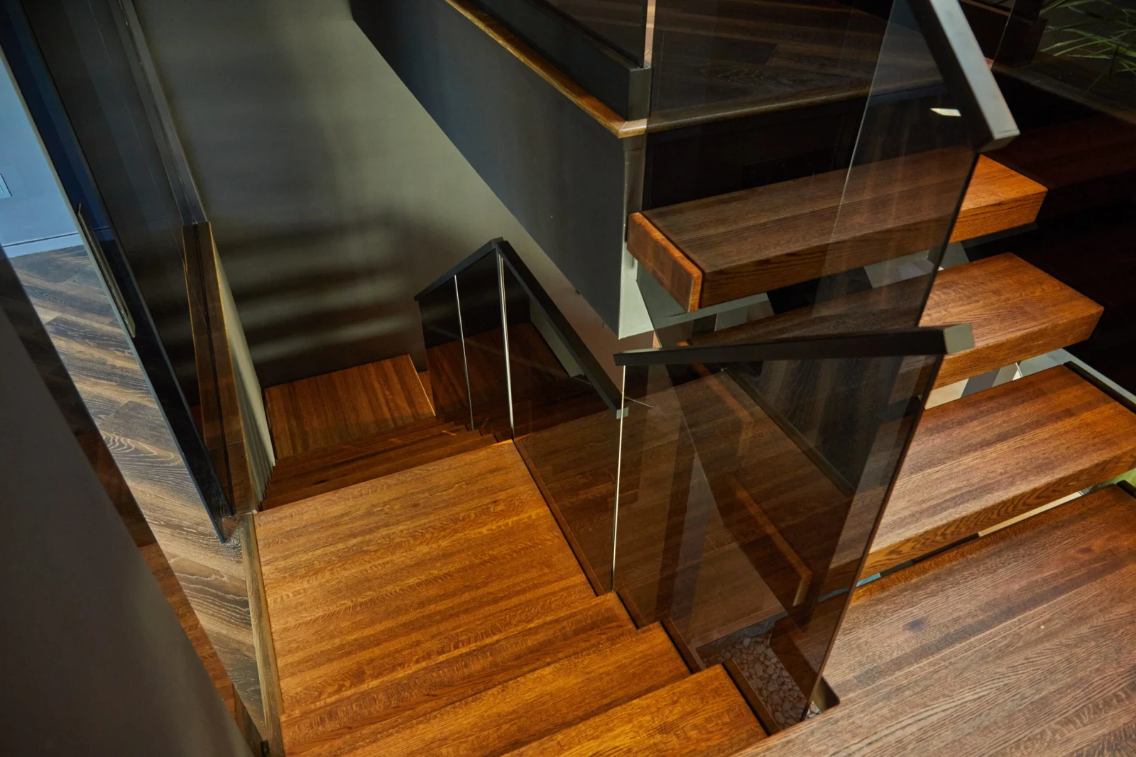 Close overhead of brown treads meeting a landing behind tinted glass panels