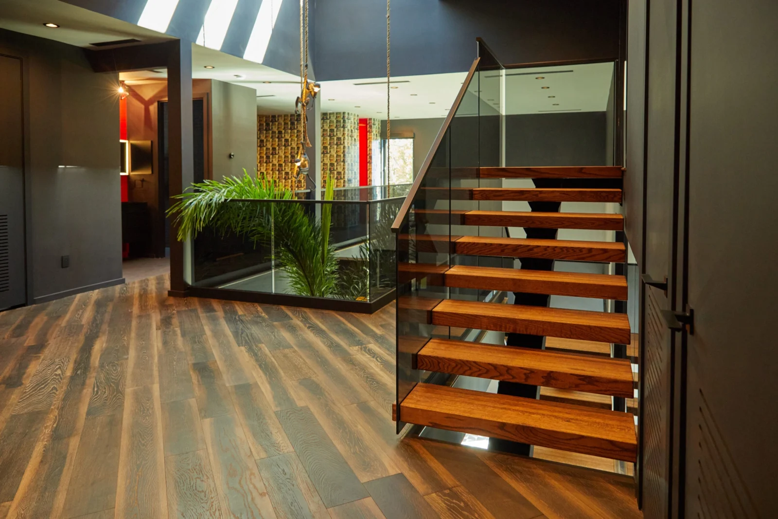 Stair rising beside an indoor planter under a skylight above wide-plank flooring