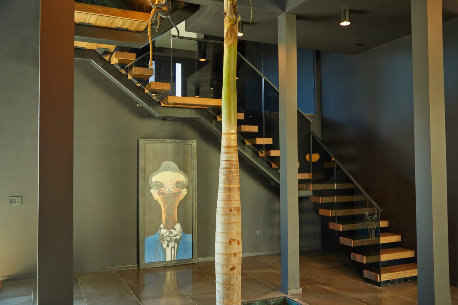 Wood treads and tinted glass railing on a switchback stair behind a slender palm trunk