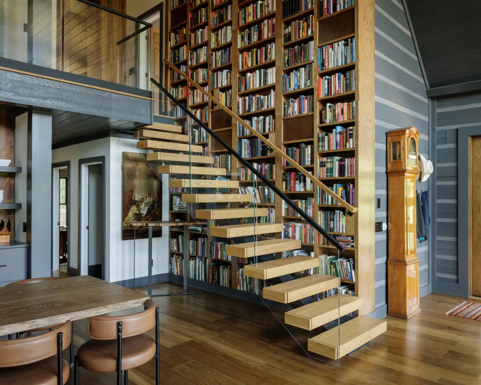 Floating stair with light treads climbing past a two-story wall of bookshelves and a glass railing