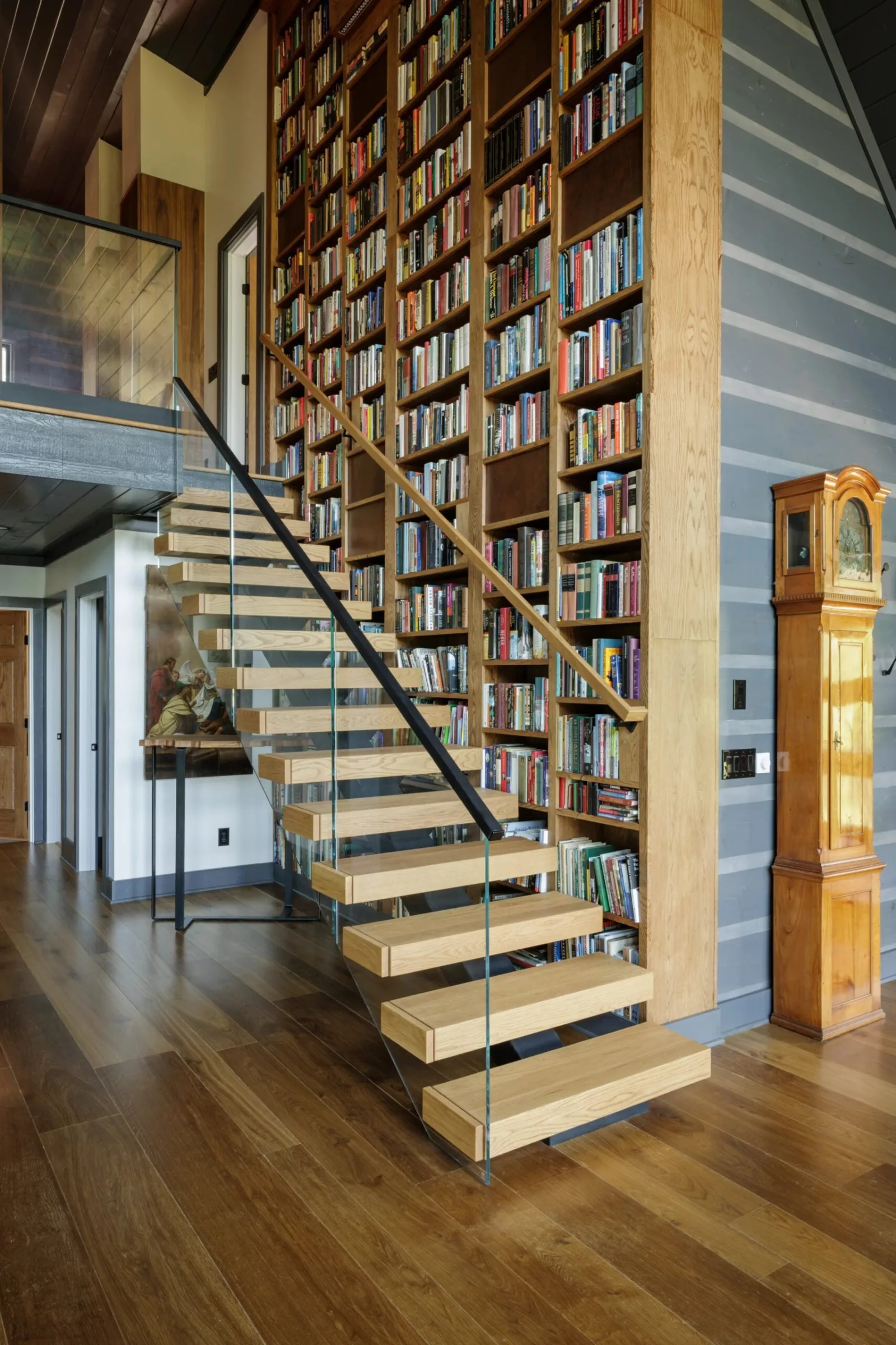 Stair with light treads and glass railing set against a two-story library wall
