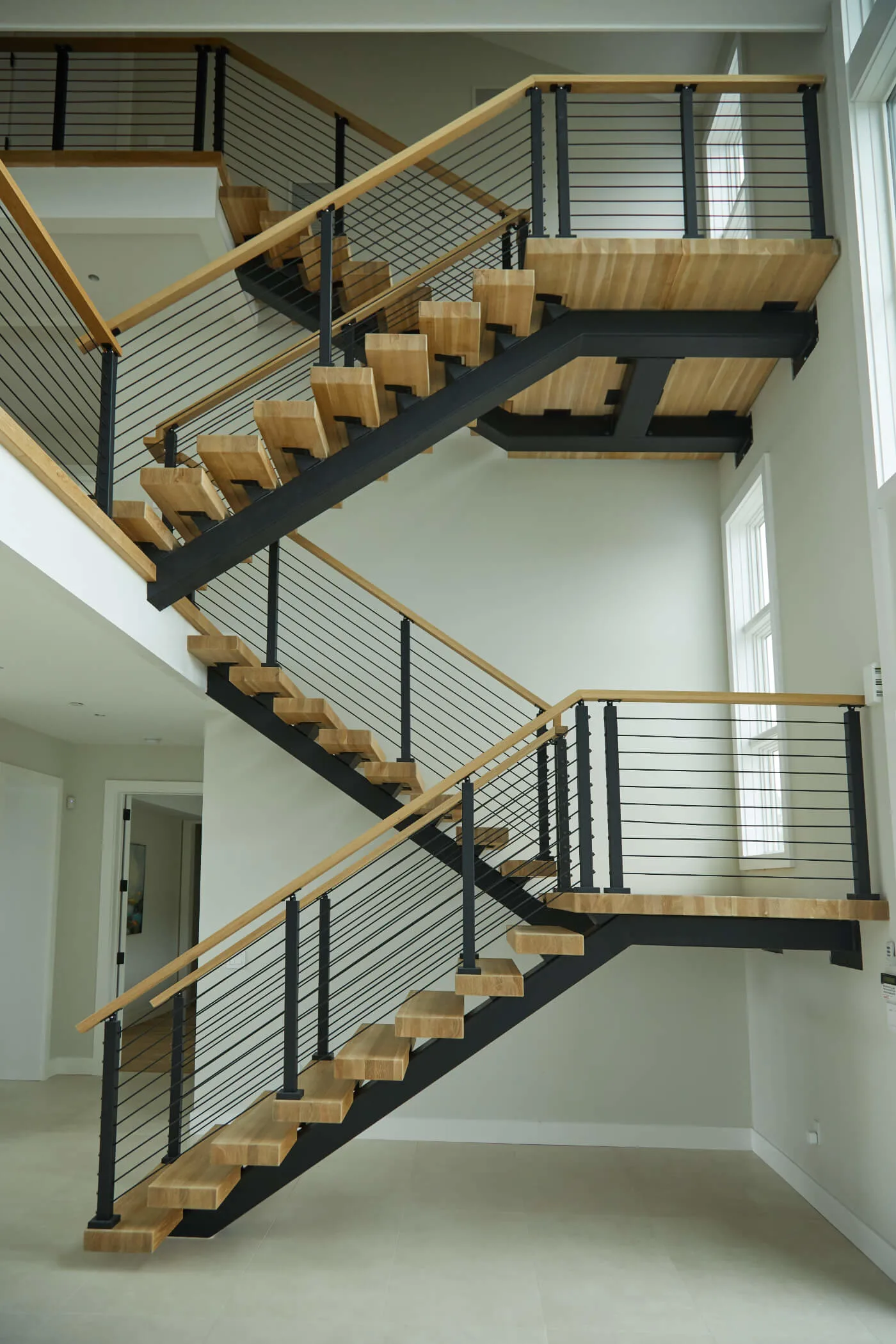 Multi-level switchback flight with black stringers and rod railing on white walls
