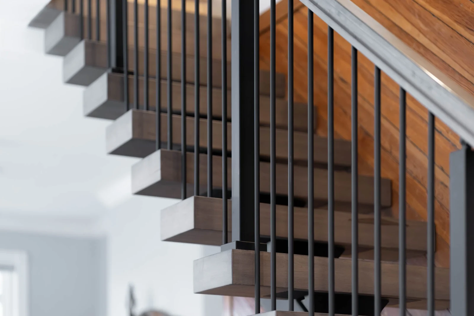Close view of vertical black rods beside cantilevered tread ends under a wood plank ceiling