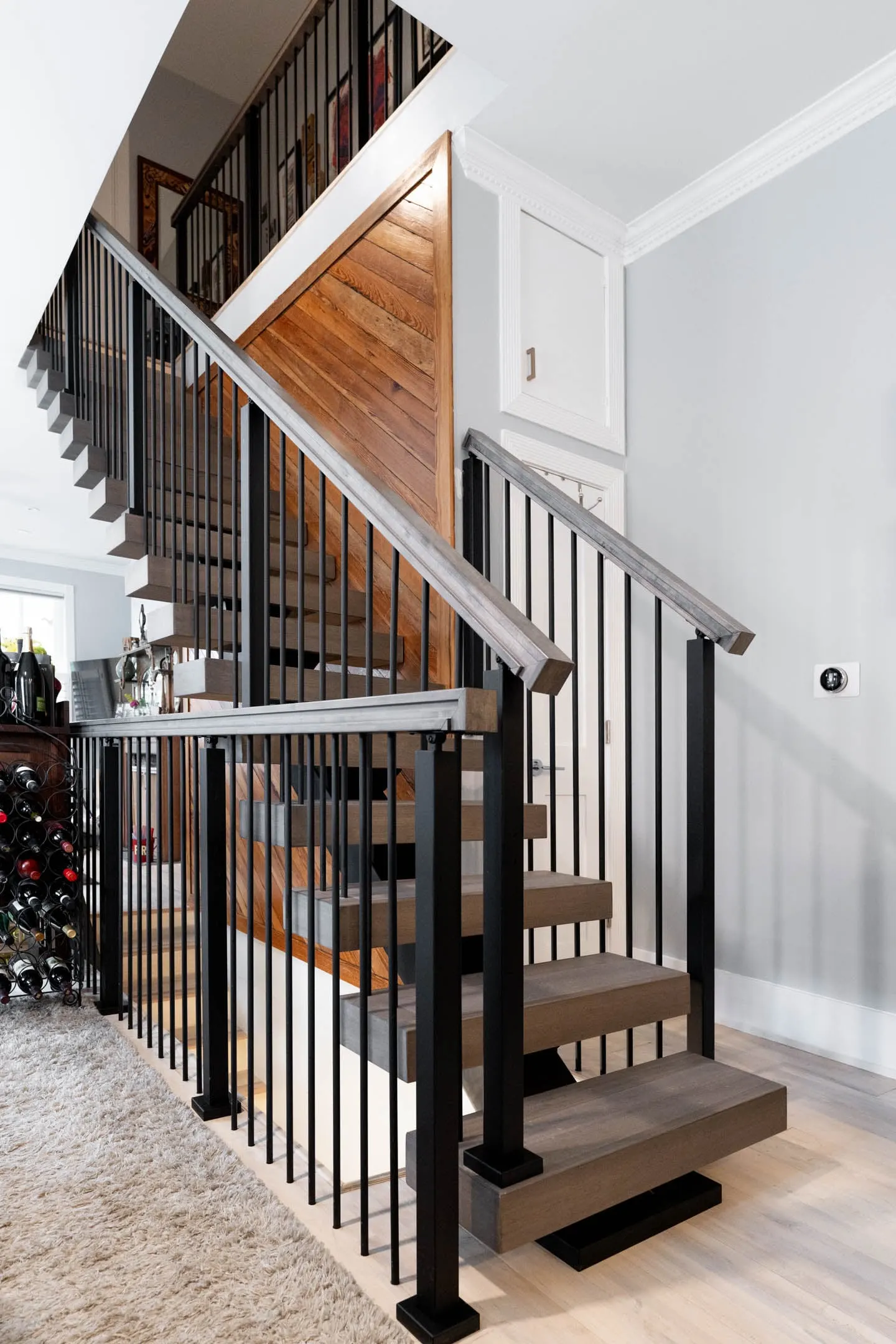 Stair with vertical black rod infill and gray treads beside a plank wall
