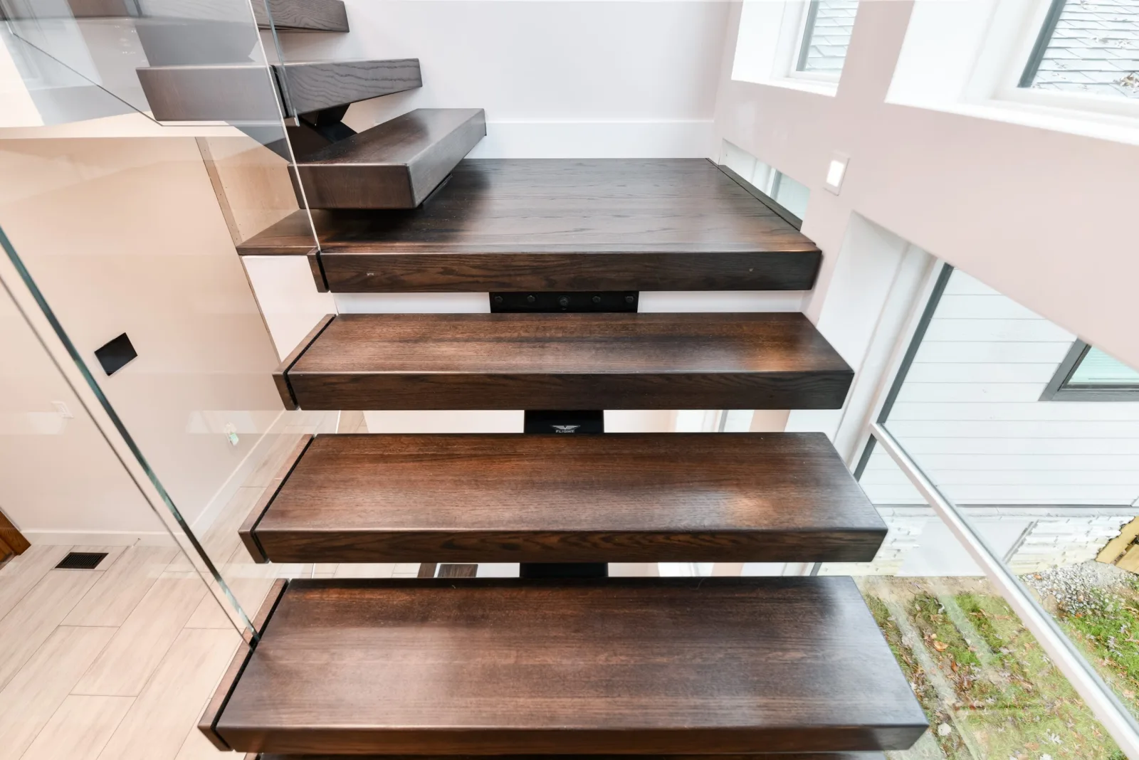 Close view of dark cantilevered treads beside a frameless glass panel