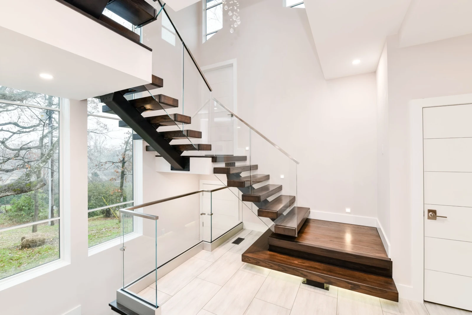 Dark treads float above a wood landing platform with frameless glass panels and slim handrail
