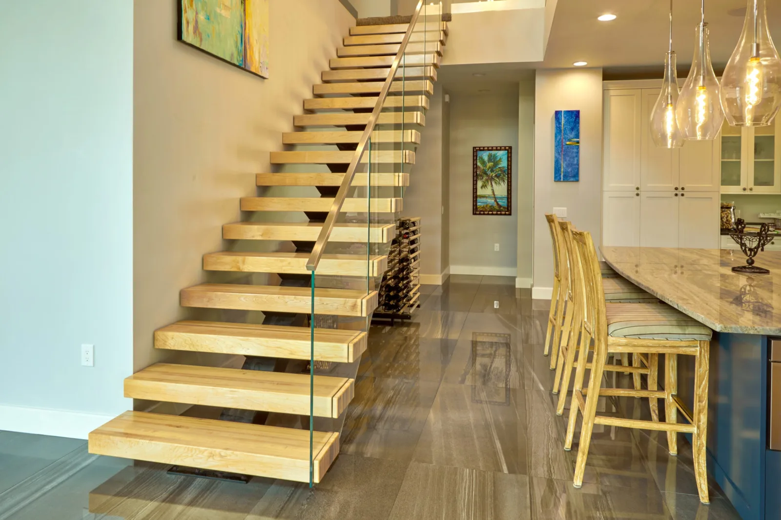 Floating stair with light wood treads and glass railing beside a kitchen island