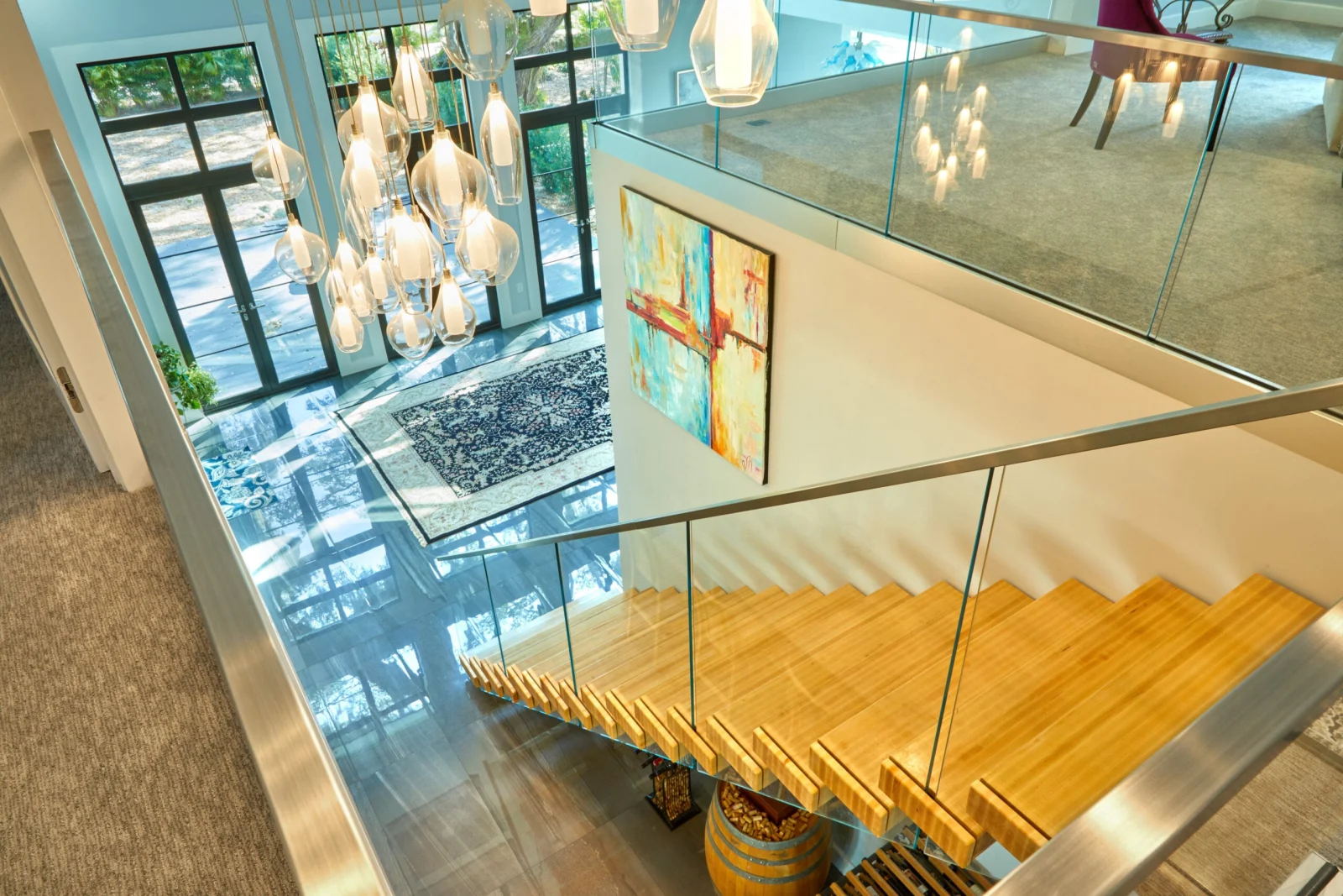 Overhead view down the stairwell past glass balcony railing and cascading pendant lights