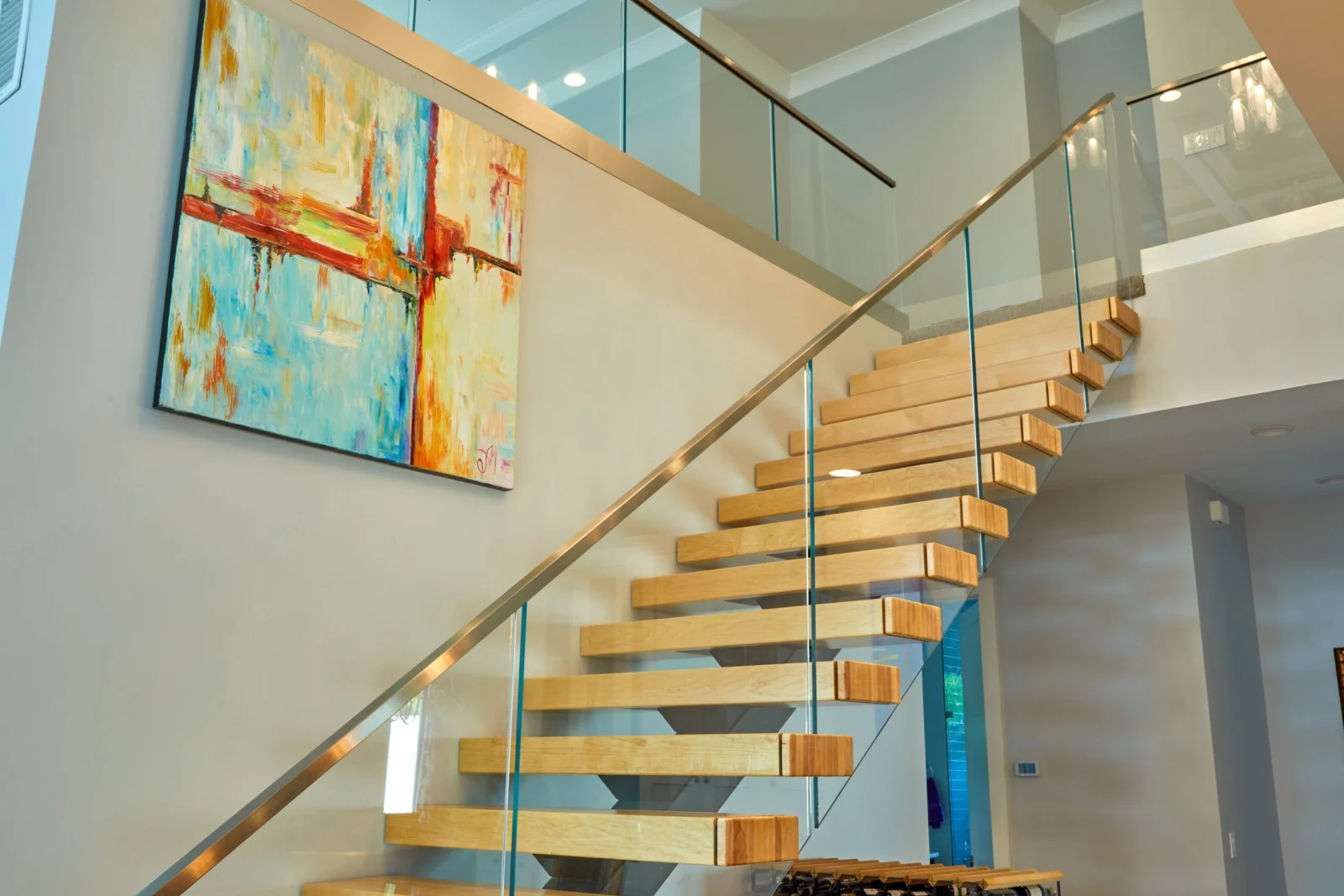 Looking up at cantilevered treads, frameless glass and a curved metal cap rail beside bright artwork