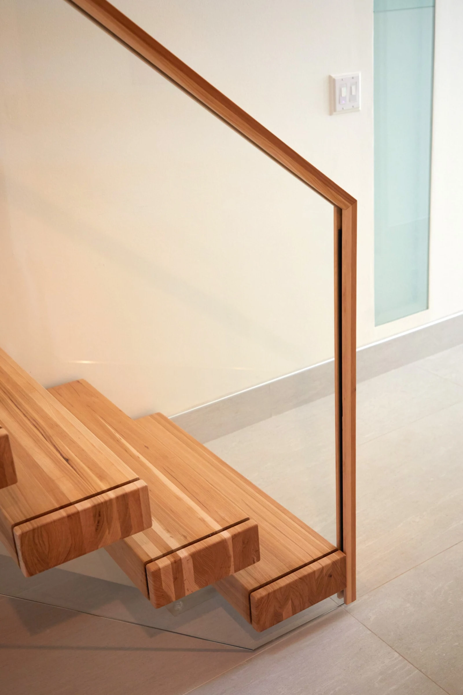 Bottom treads meeting the floor beside a glass panel framed in wood