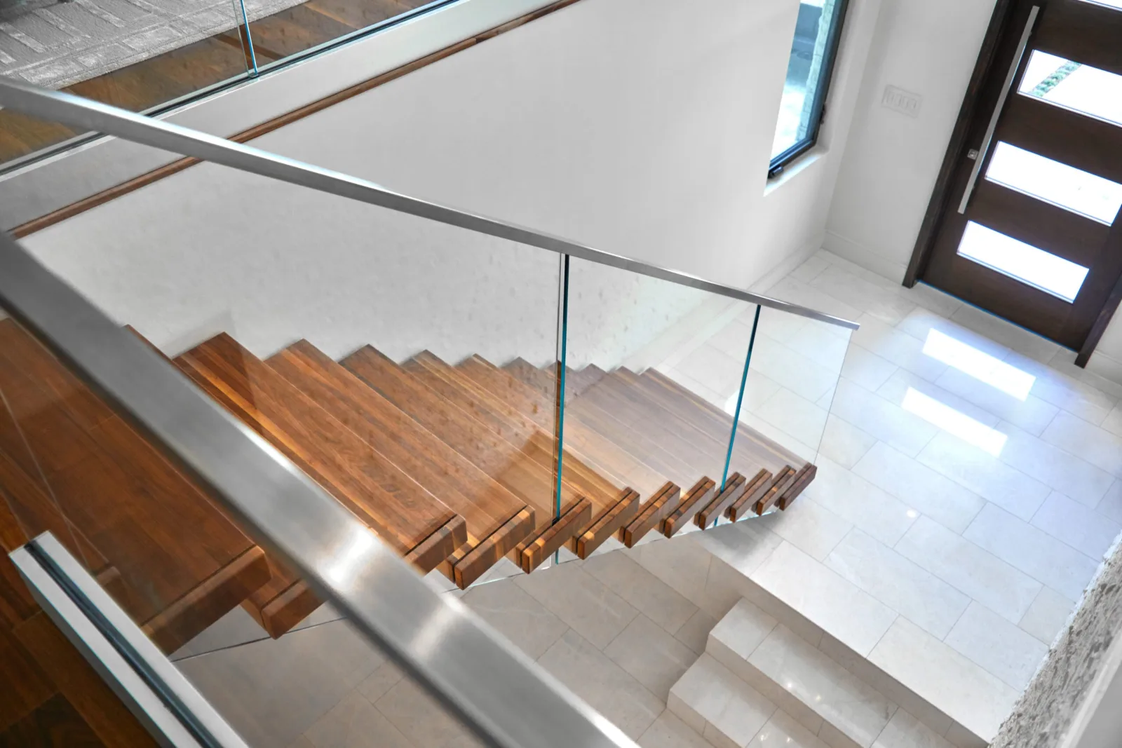 Overhead angle down a wood-tread stair to a stone entry framed by glass railing