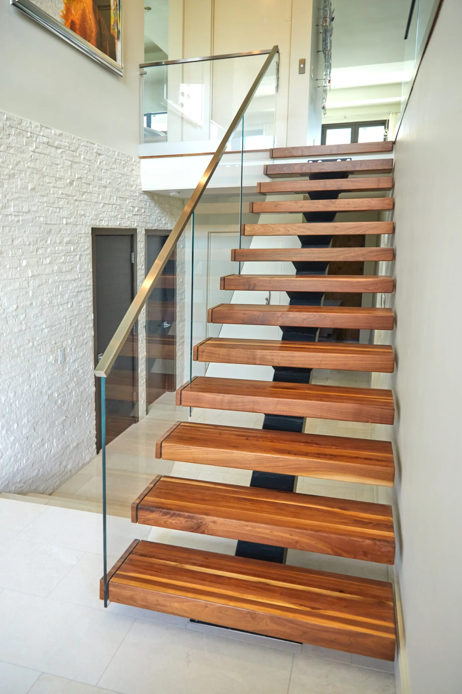 Straight view up dark-stained wood treads framed by glass railing panels