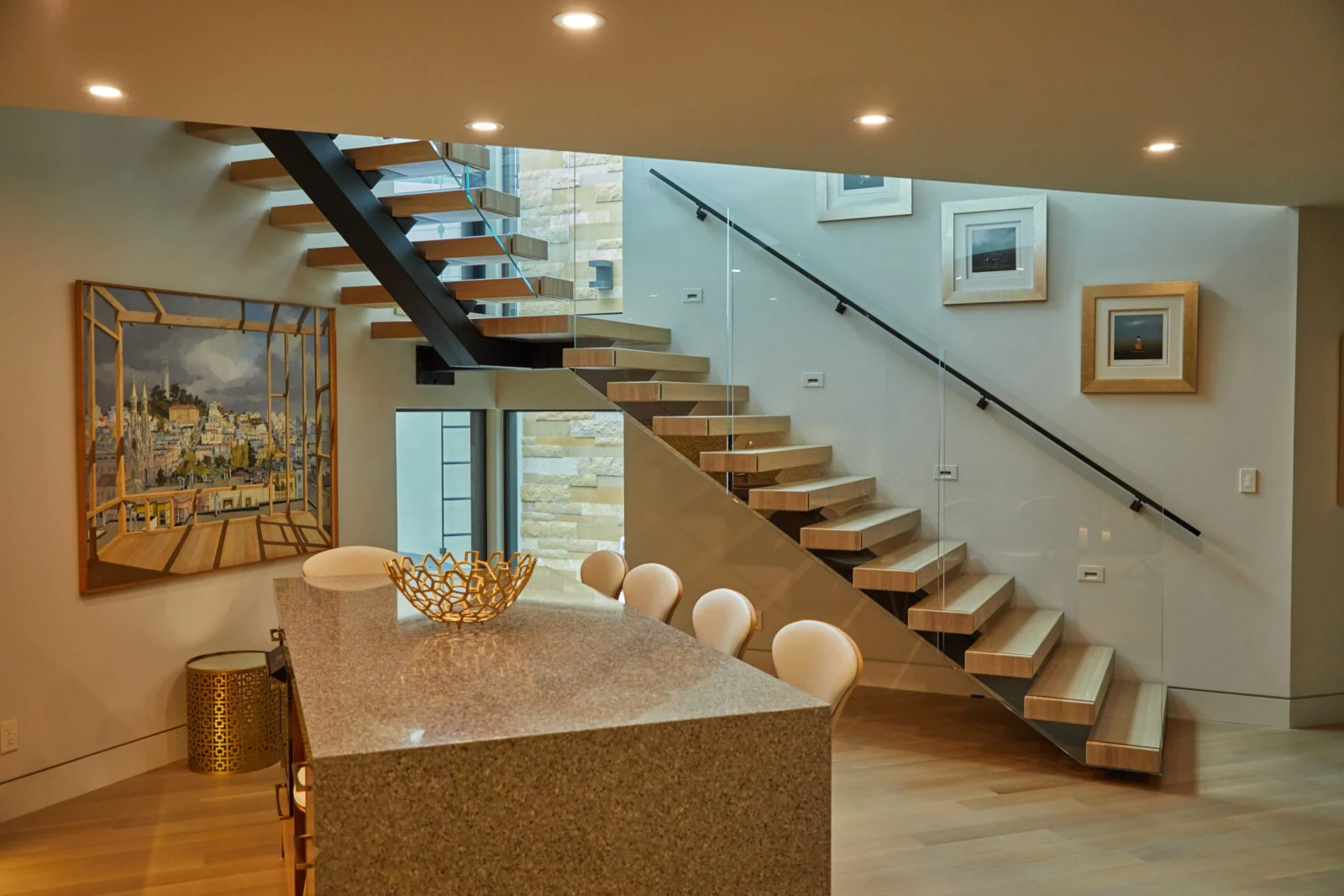 Floating stair on a black stringer with glass railing rising behind a stone kitchen island