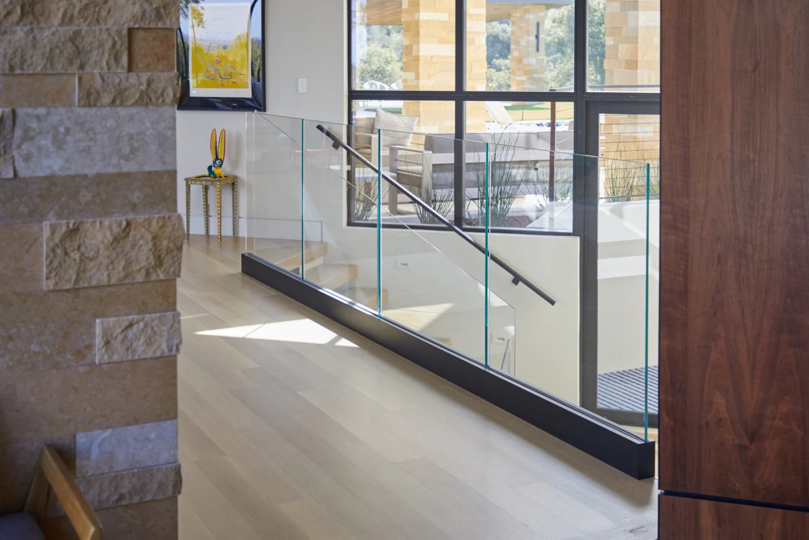 Glass railing with a black handrail sloping along the landing edge
