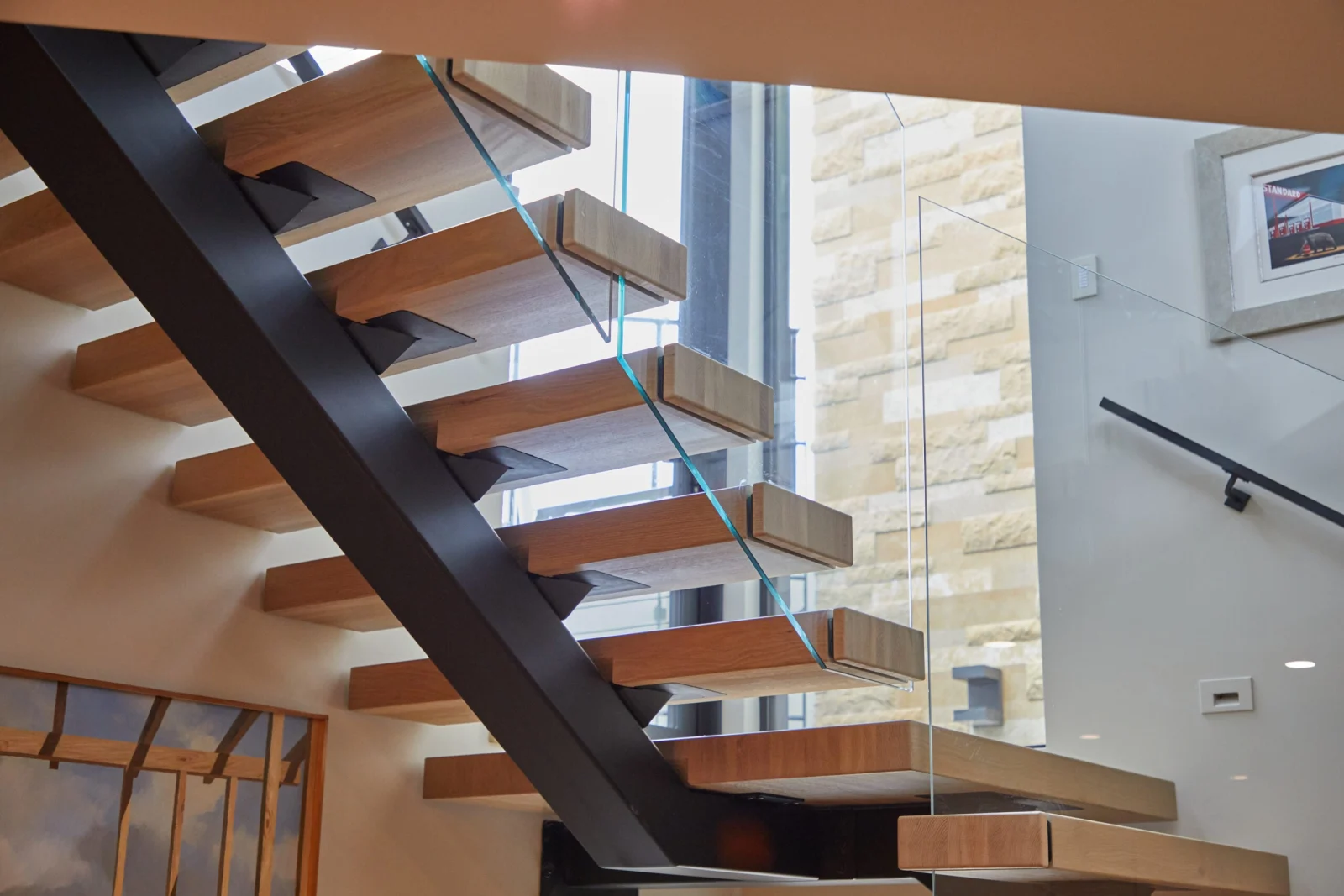 Cantilevered treads on a black center stringer against a stone feature wall