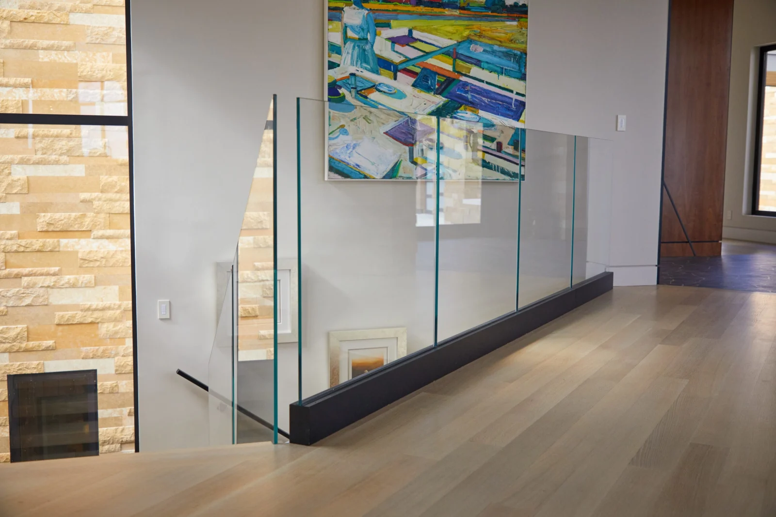 Long glass railing run in a black shoe beside a stone fireplace wall