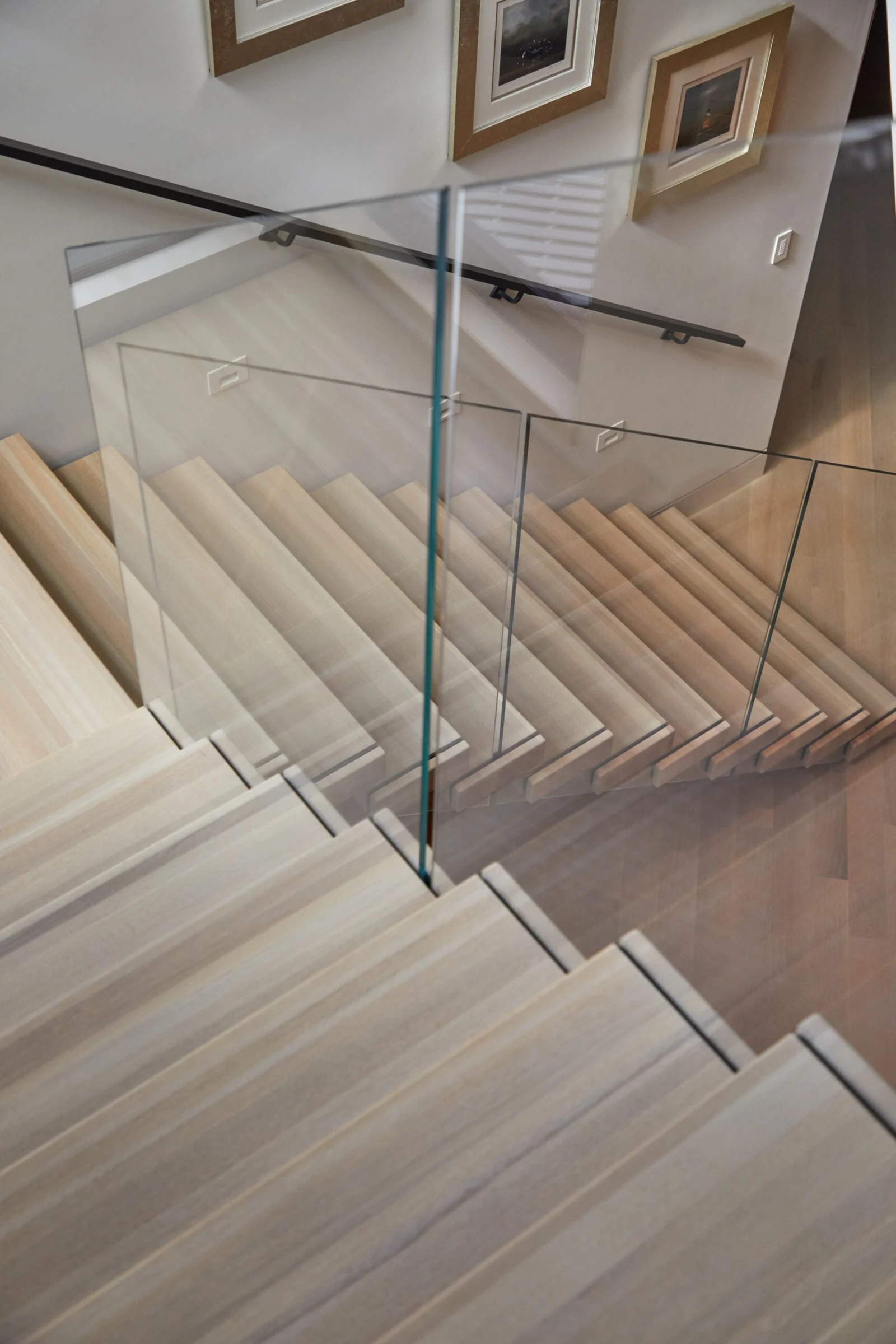 Looking down the pale treads past glass panels and a gallery wall