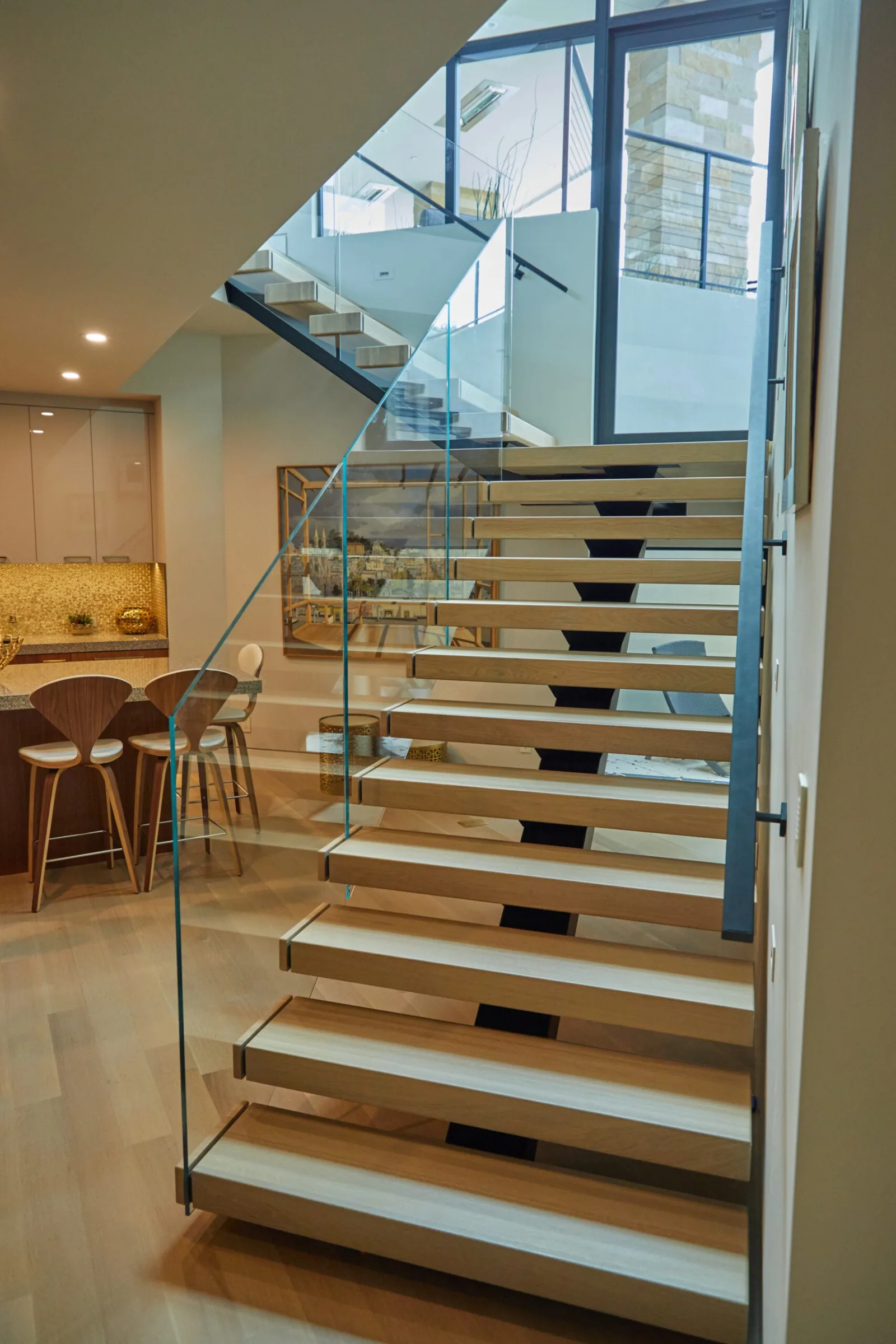 View up pale wood treads with the kitchen visible beyond the glass