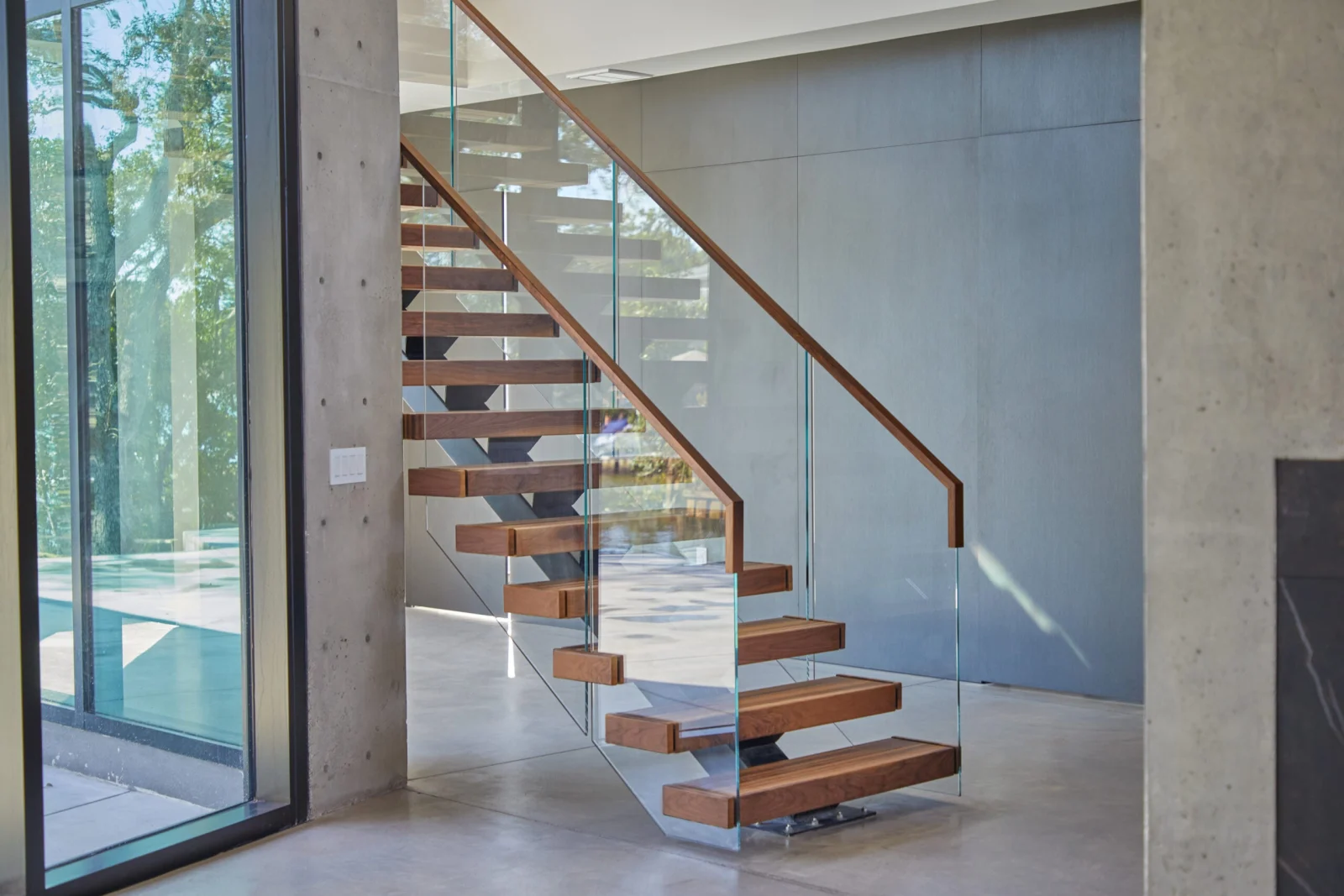 Side view of dark-stained treads and glass railing on a concrete wall