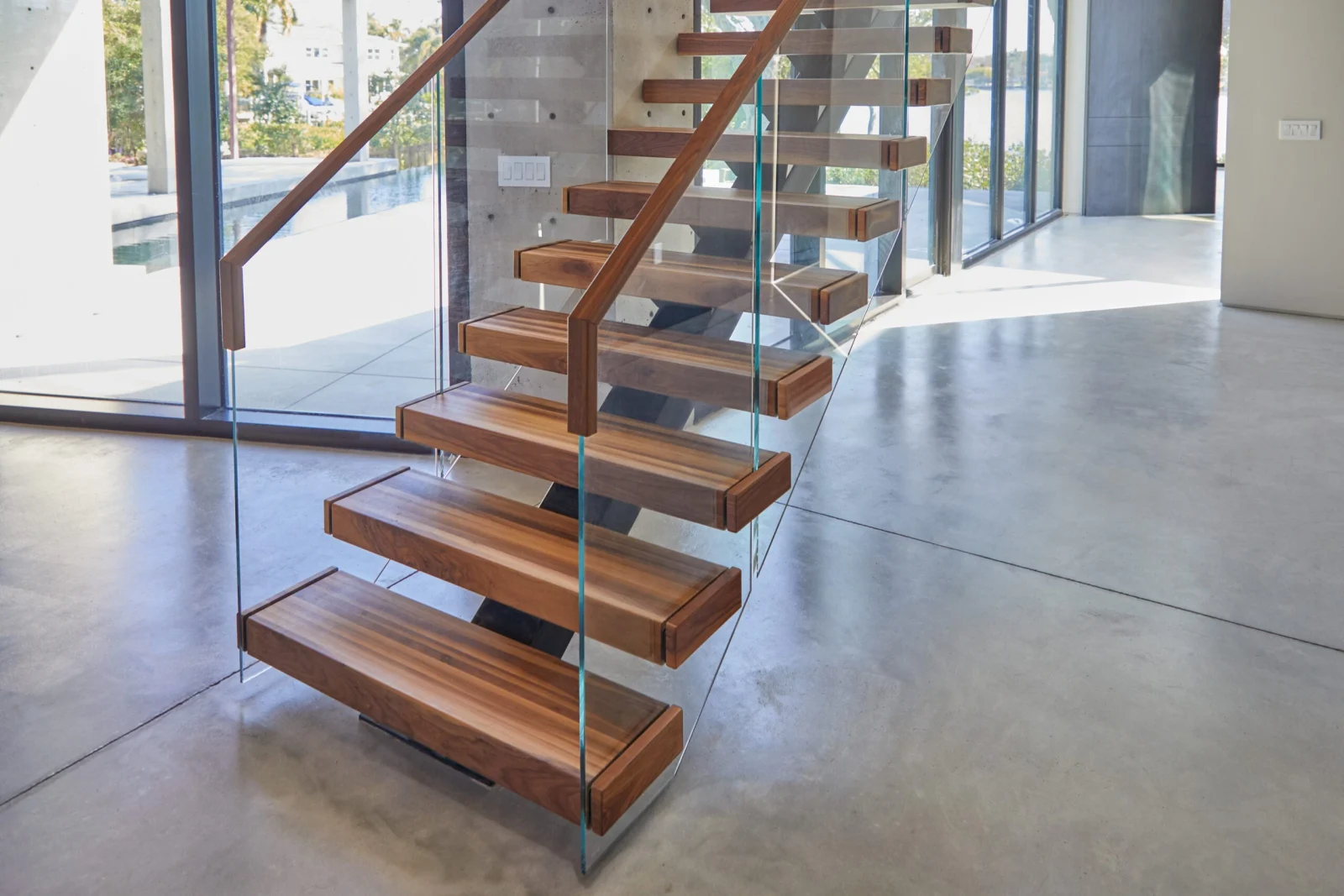 Warm brown treads cantilevered over polished concrete with frameless glass and a wood handrail