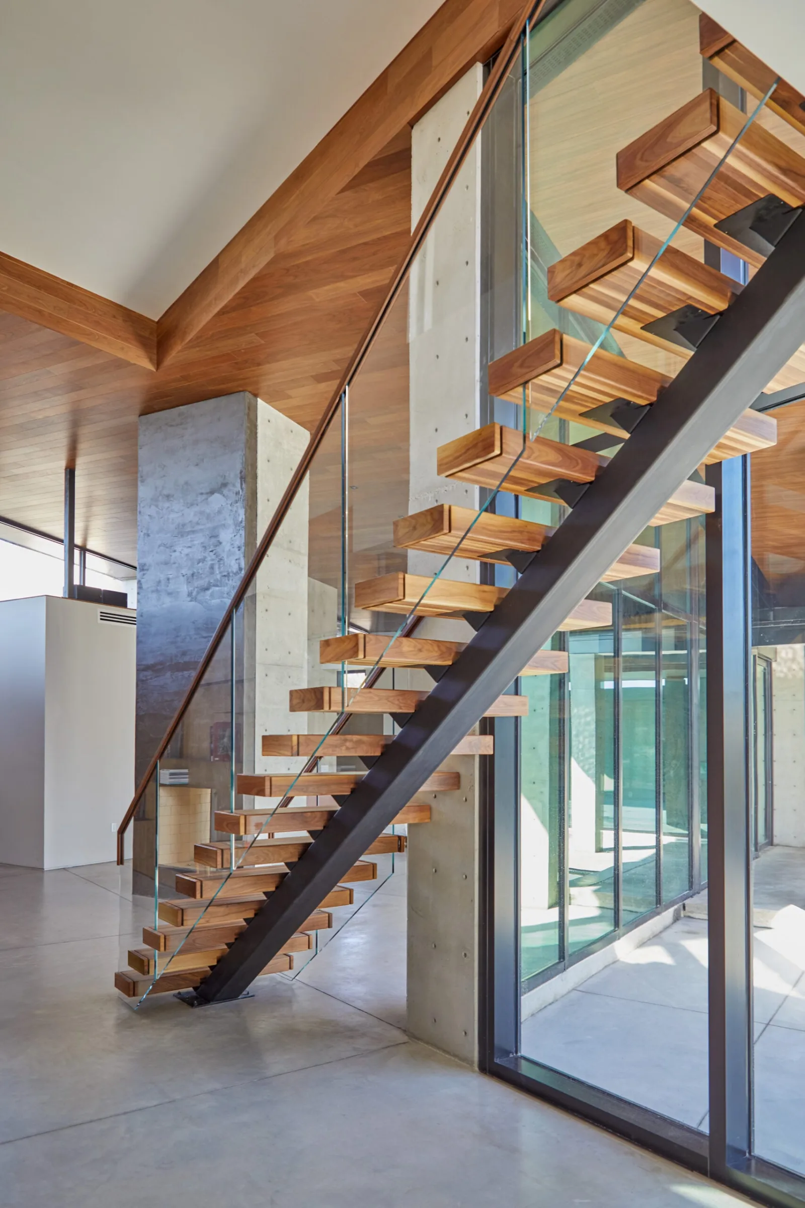 Treads and glass railing seen from below against a wood plank ceiling