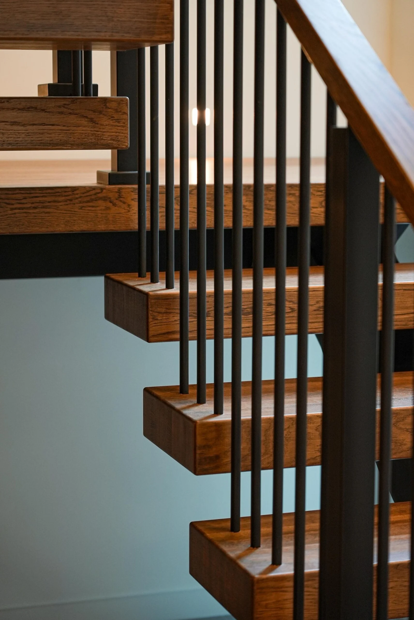 Cantilevered wood treads behind slim black balusters and a wood handrail