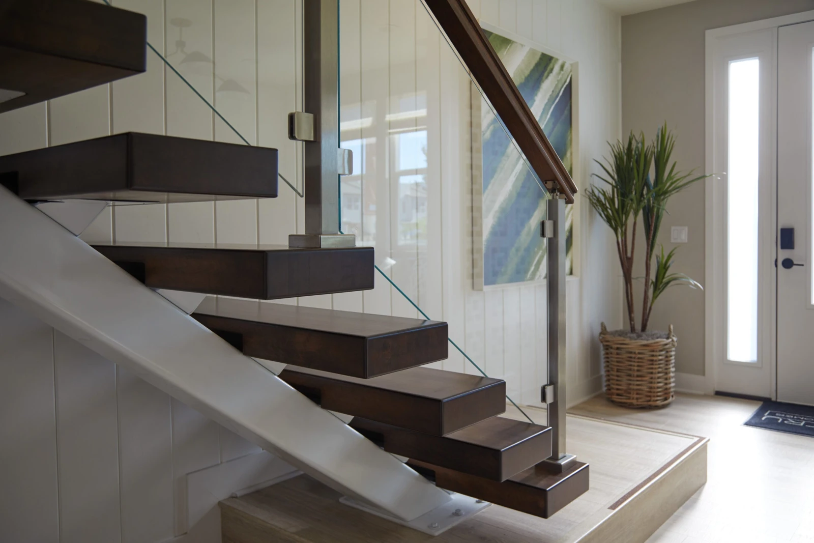 Dark treads cantilever from a white shiplap wall behind frameless glass and a wood handrail