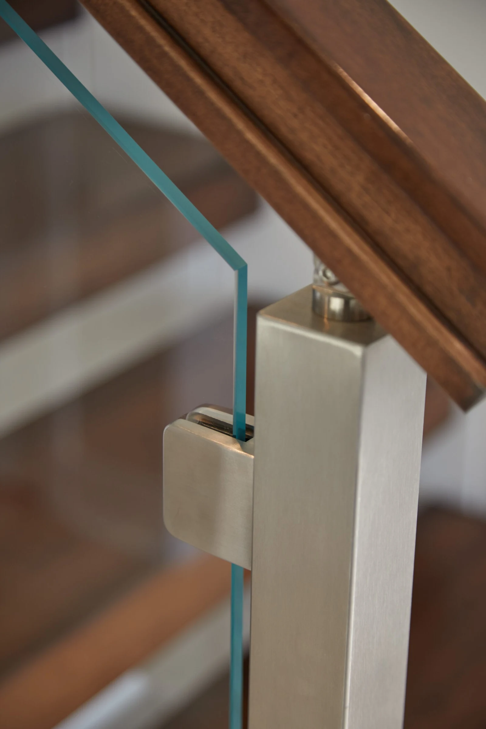 Detail of a glass panel clamp and post cap where the wood handrail lands