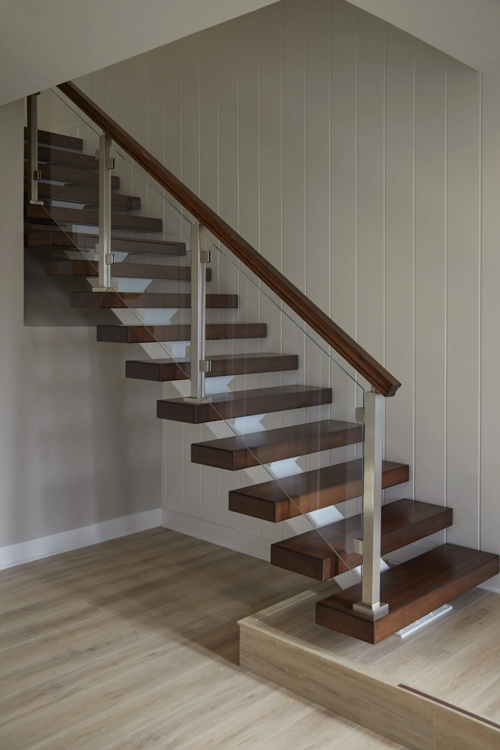 Straight floating stair with dark wood treads and glass railing against a white paneled wall
