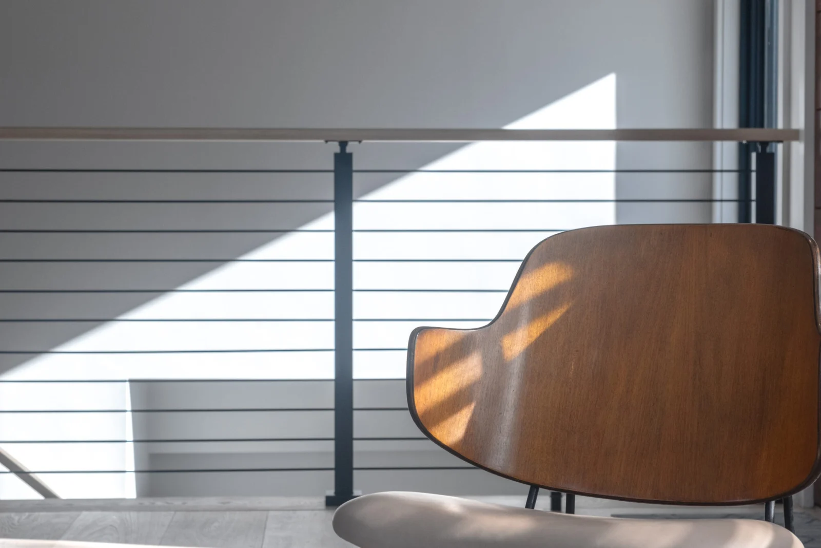 Sunlight striping a run of black horizontal rods behind a molded chair