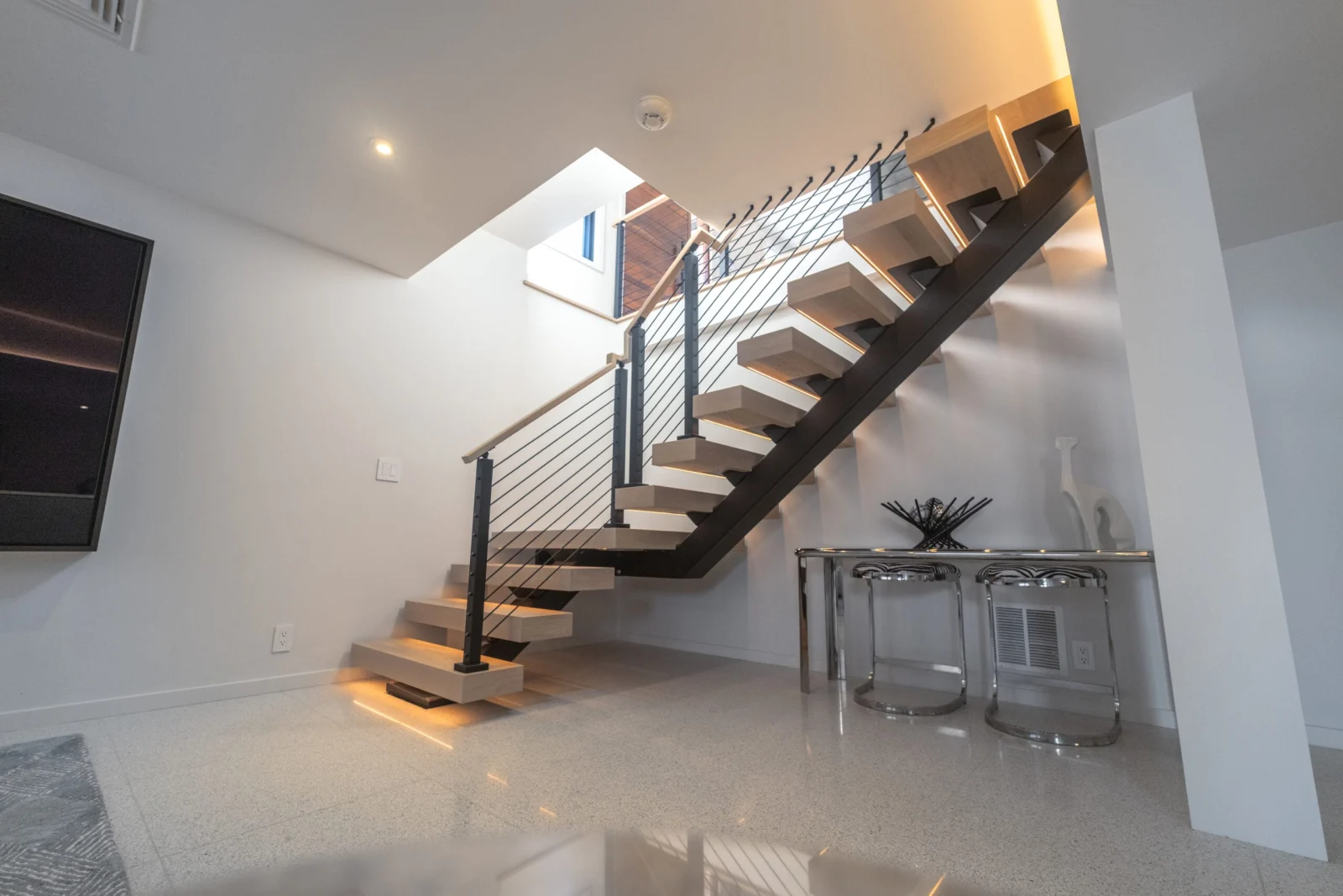 Floating stair with pale treads and black horizontal rod railing above a polished floor