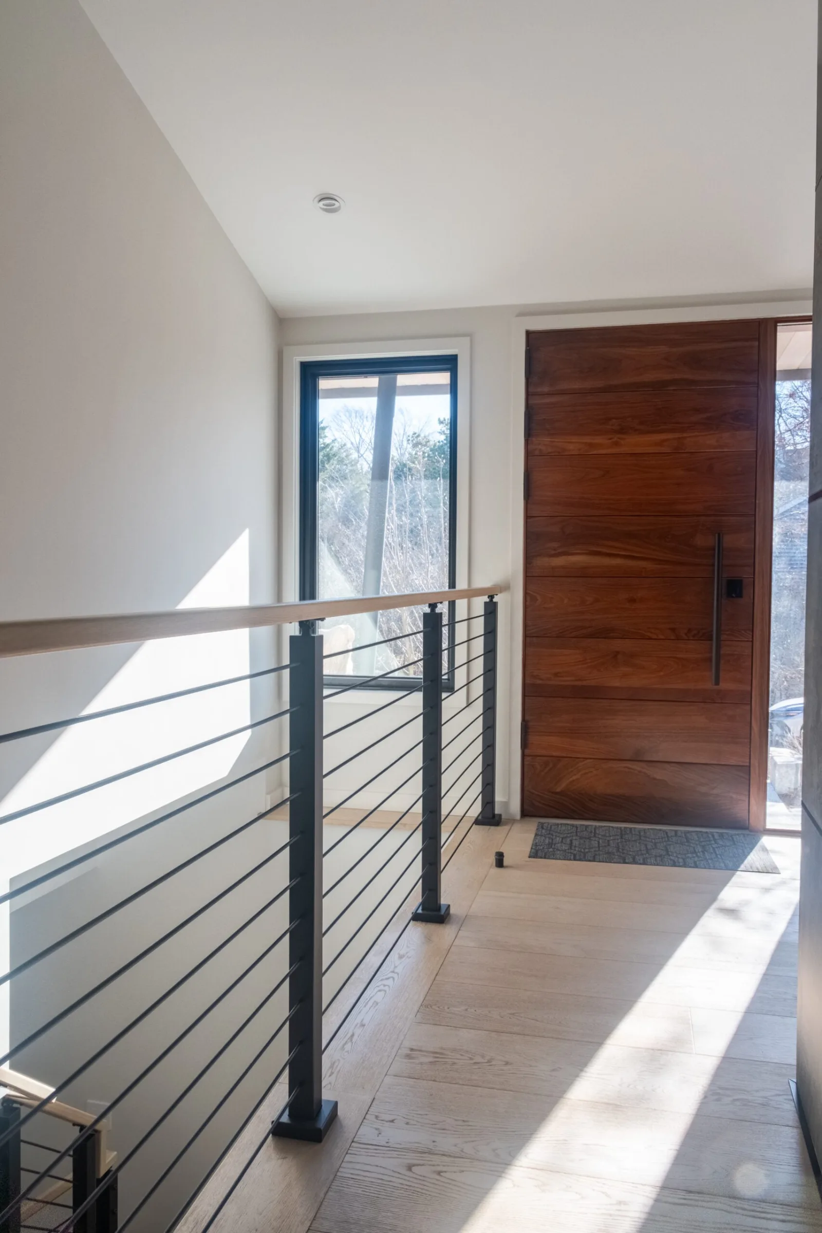 Balcony rod railing along an upper hall leading to a dark wood entry door