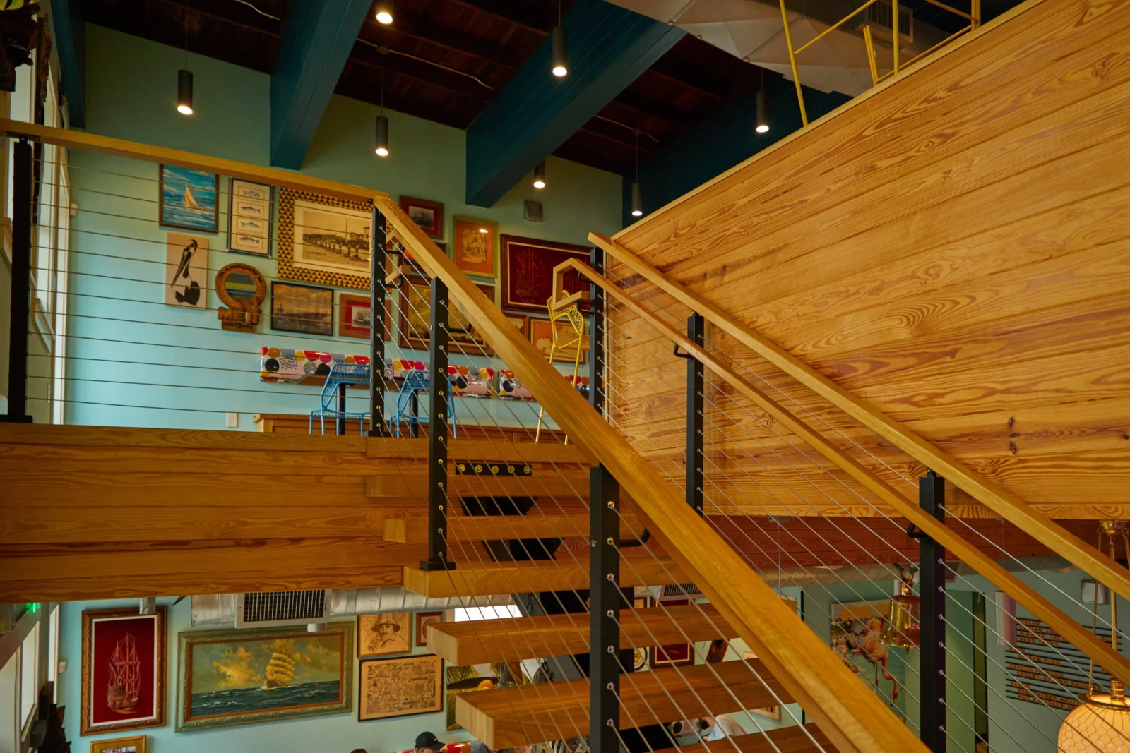 Upper walkway with cable railing beside a picture wall and wood plank ceiling