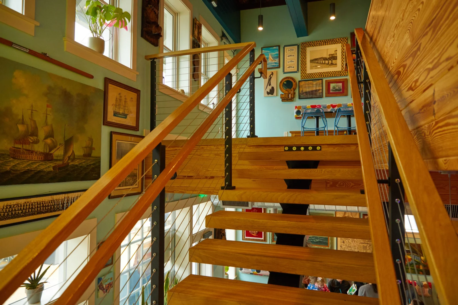 Climbing between cable railing and a wood top rail past teal walls hung with framed art