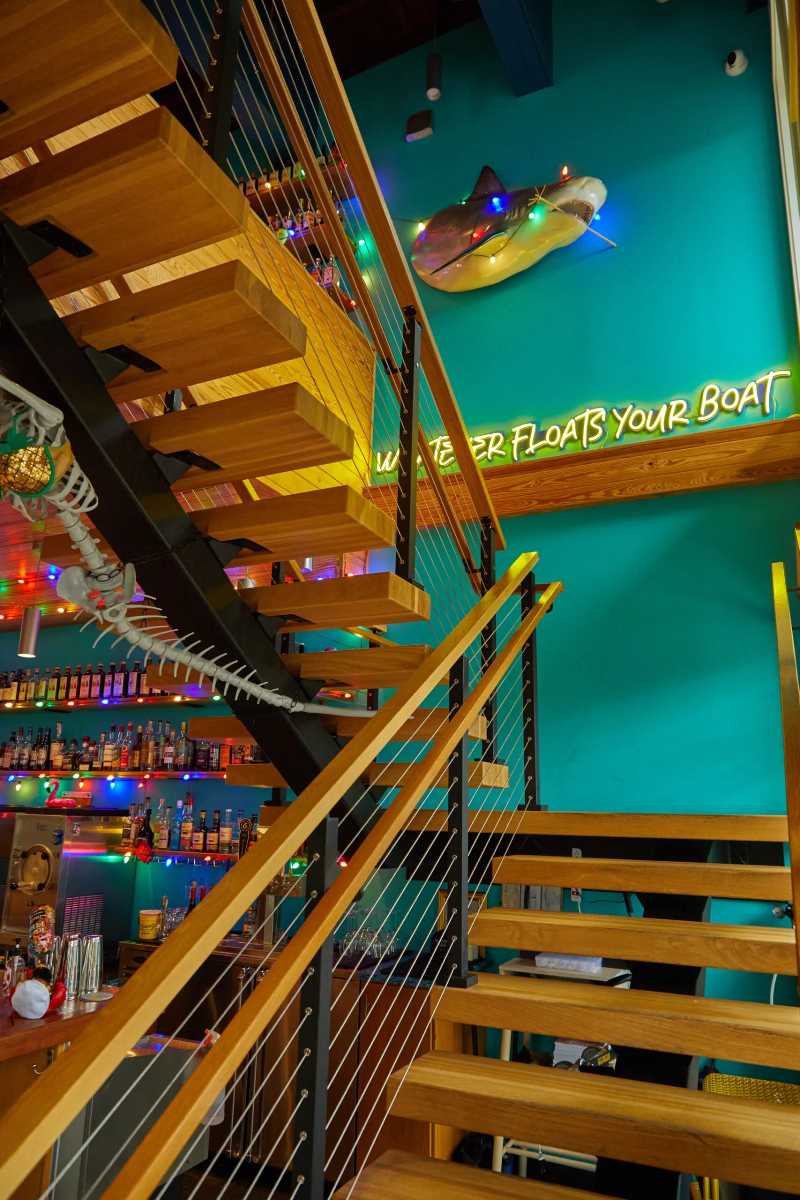 Wood treads and cable railing climbing past a neon sign on a teal wall