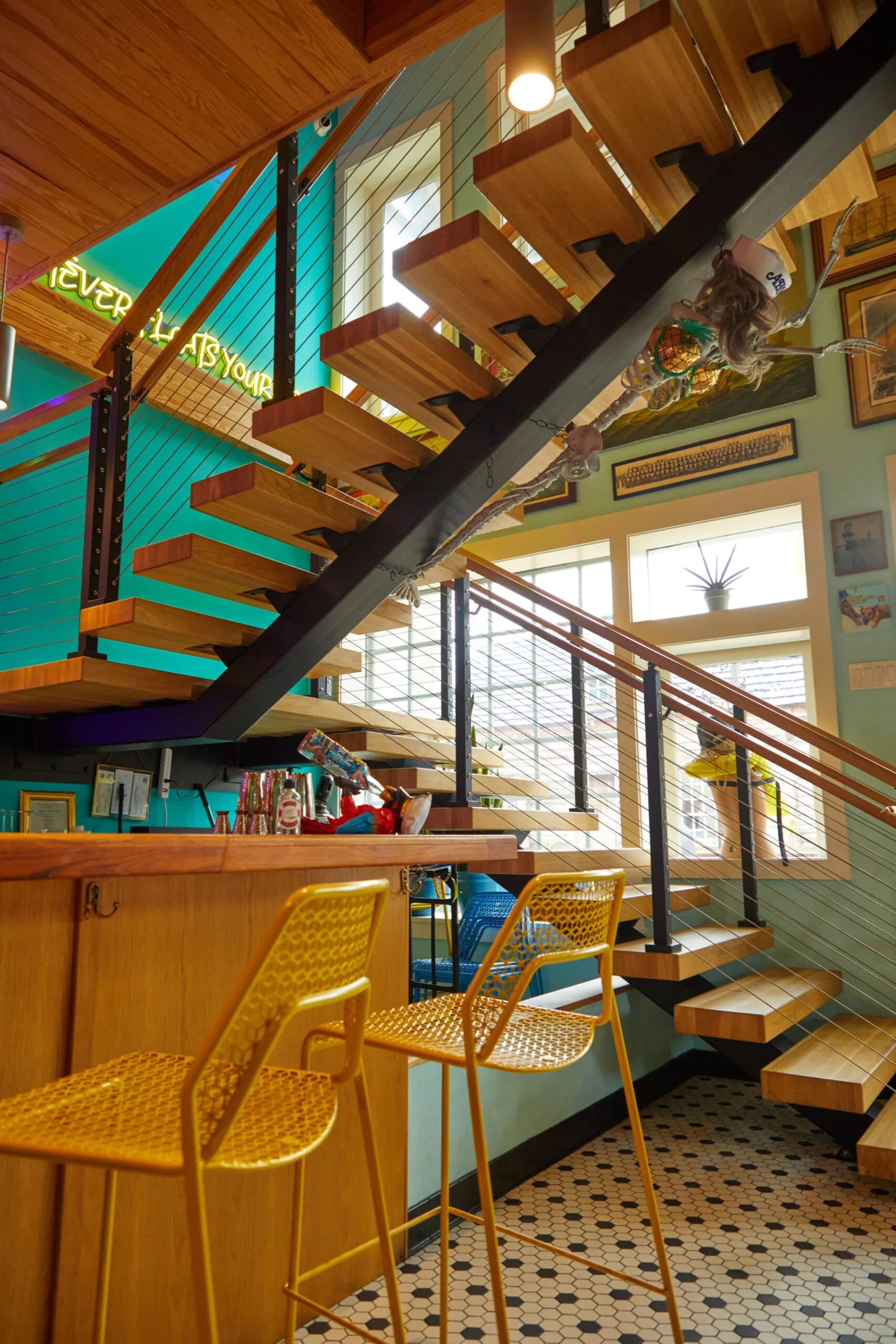Wood tread stair with cable railing rising above a bar with yellow stools