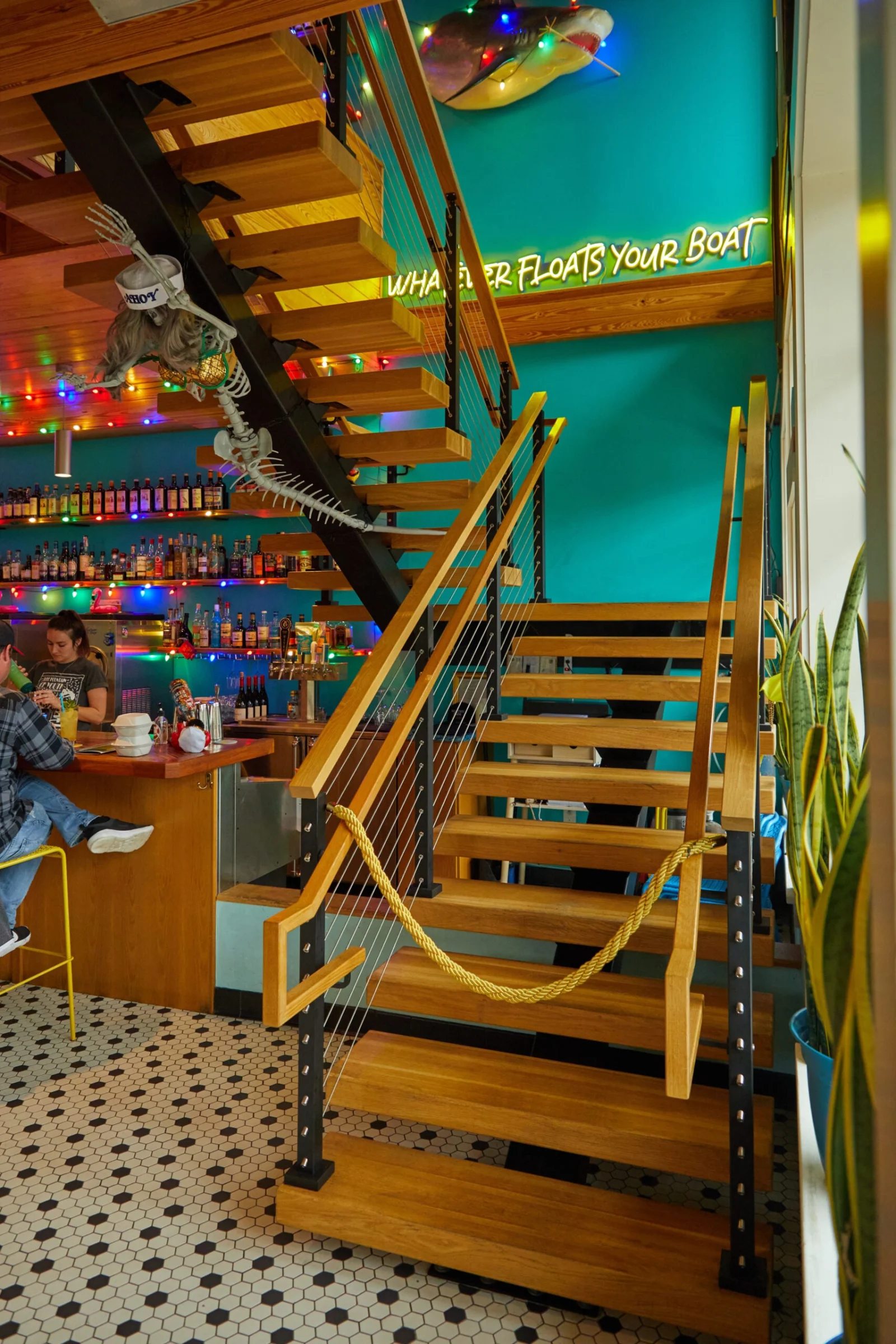 Stair base with wood handrail and cable railing beside a brightly lit bar