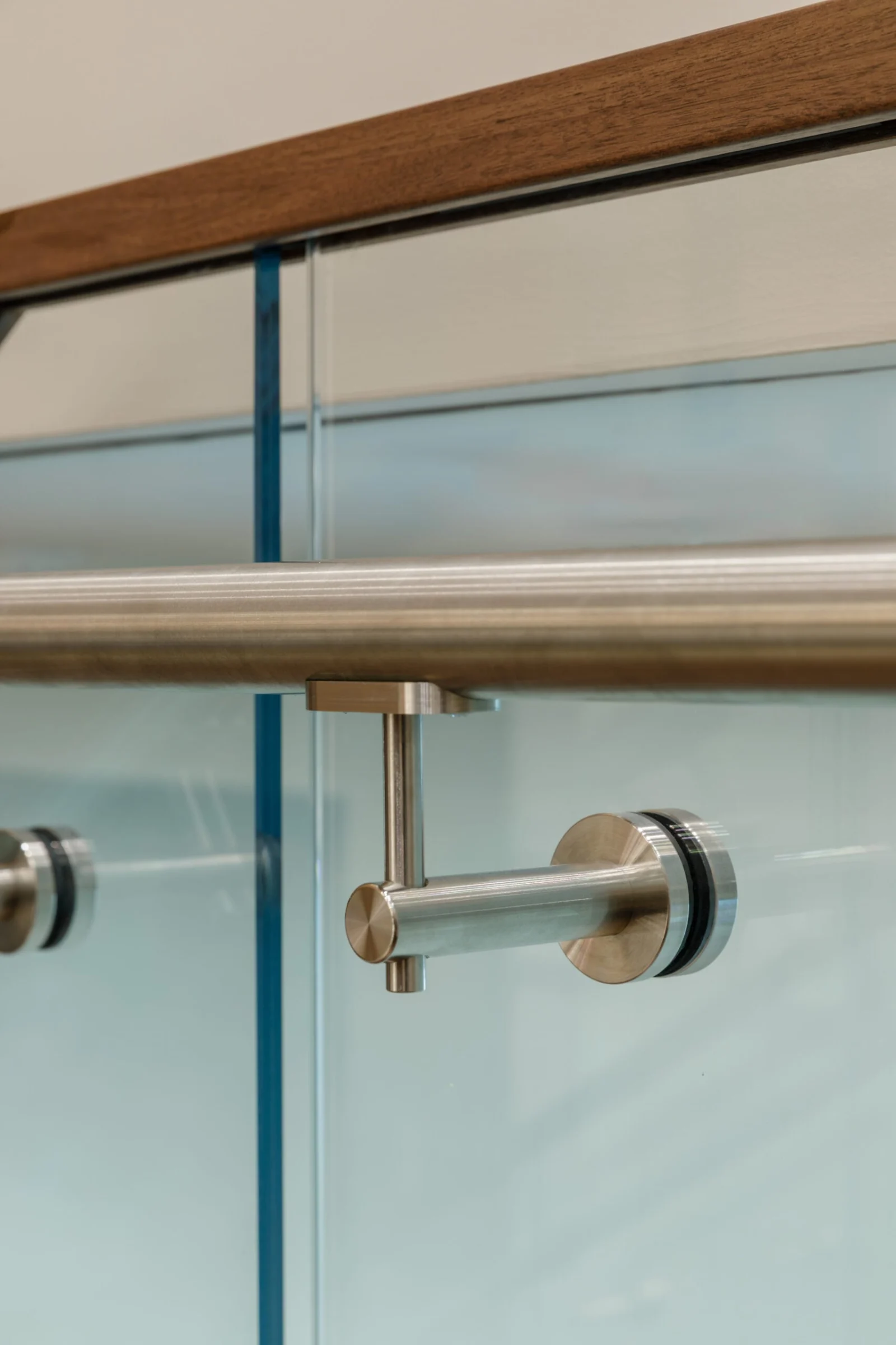 Handrail standoff and glass clamp detail on a frosted panel near the wall