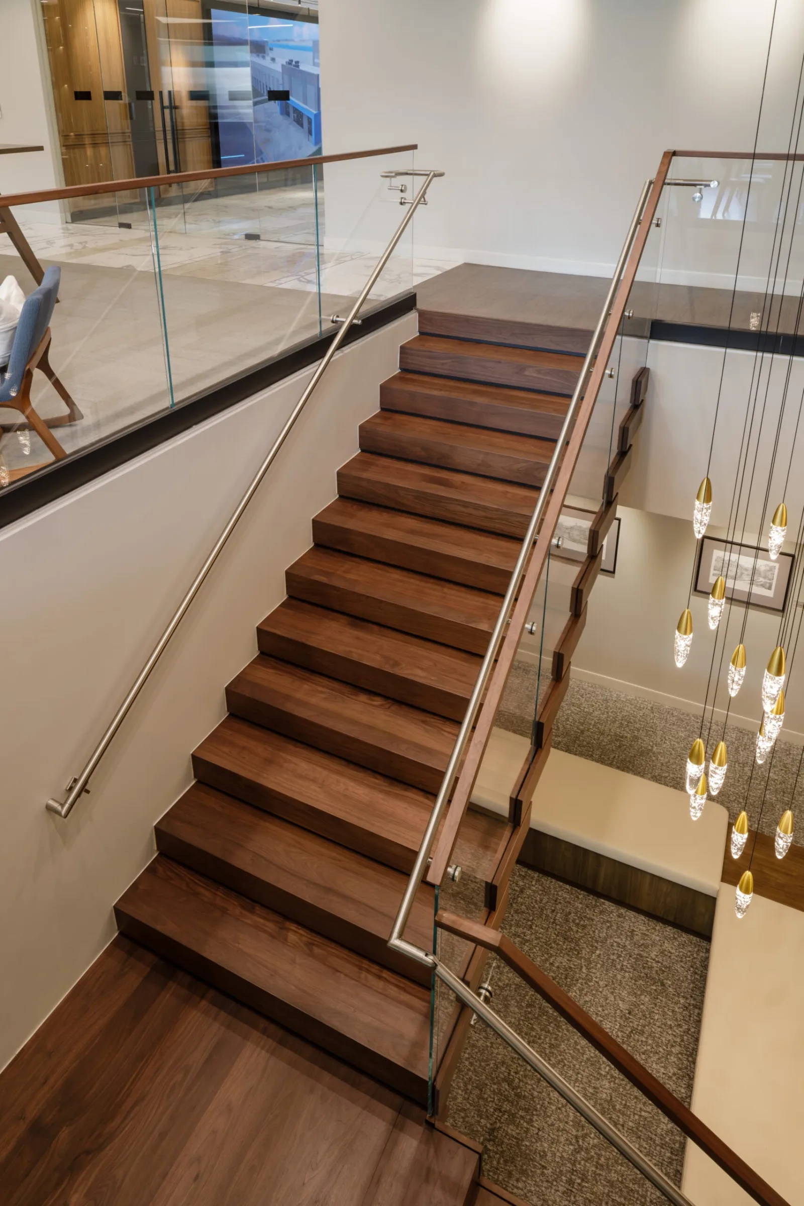 Looking down the flight of dark wood treads beside a stainless handrail