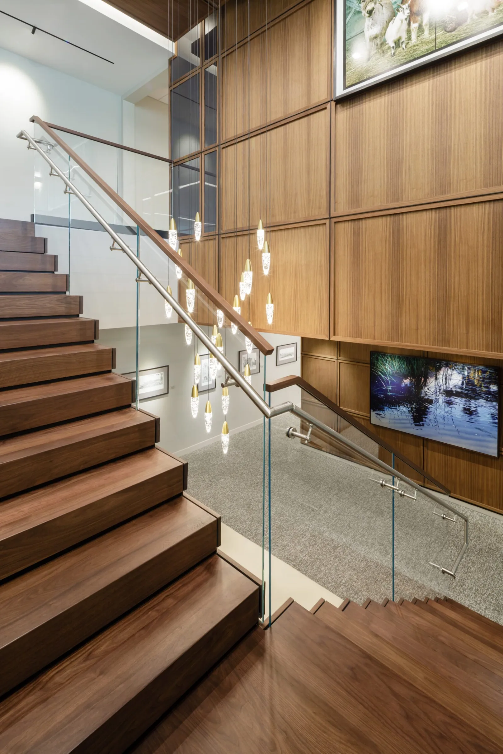 Stair rising past wood wall panels with pendant lights beyond the glass railing