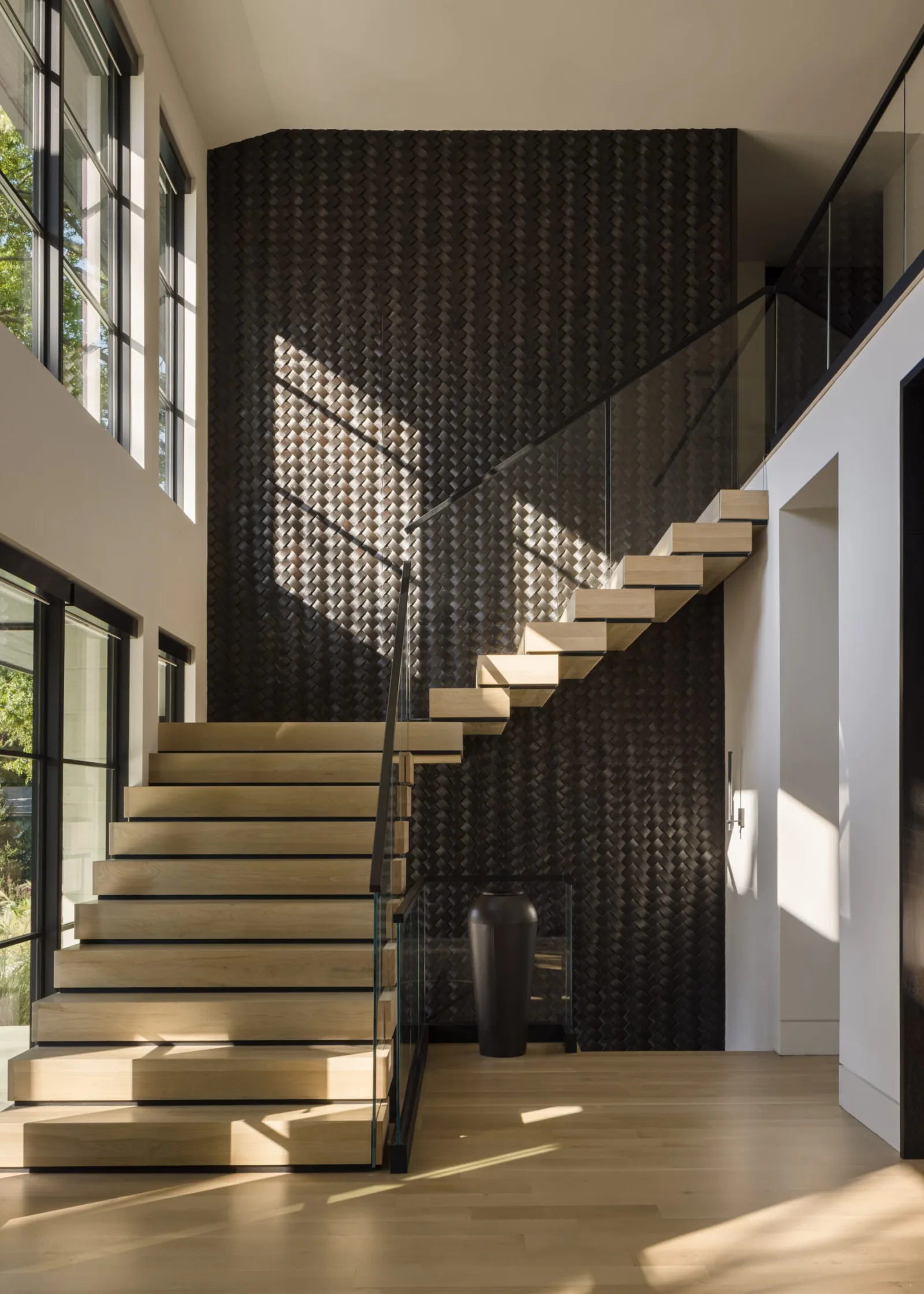 Pale treads and glass railing against a dark textured wall washed with window light