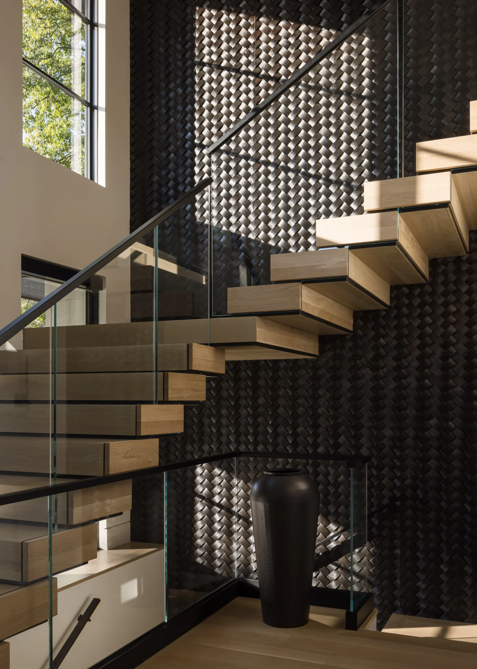 Stair turning at the landing against a dark woven wall panel and glass