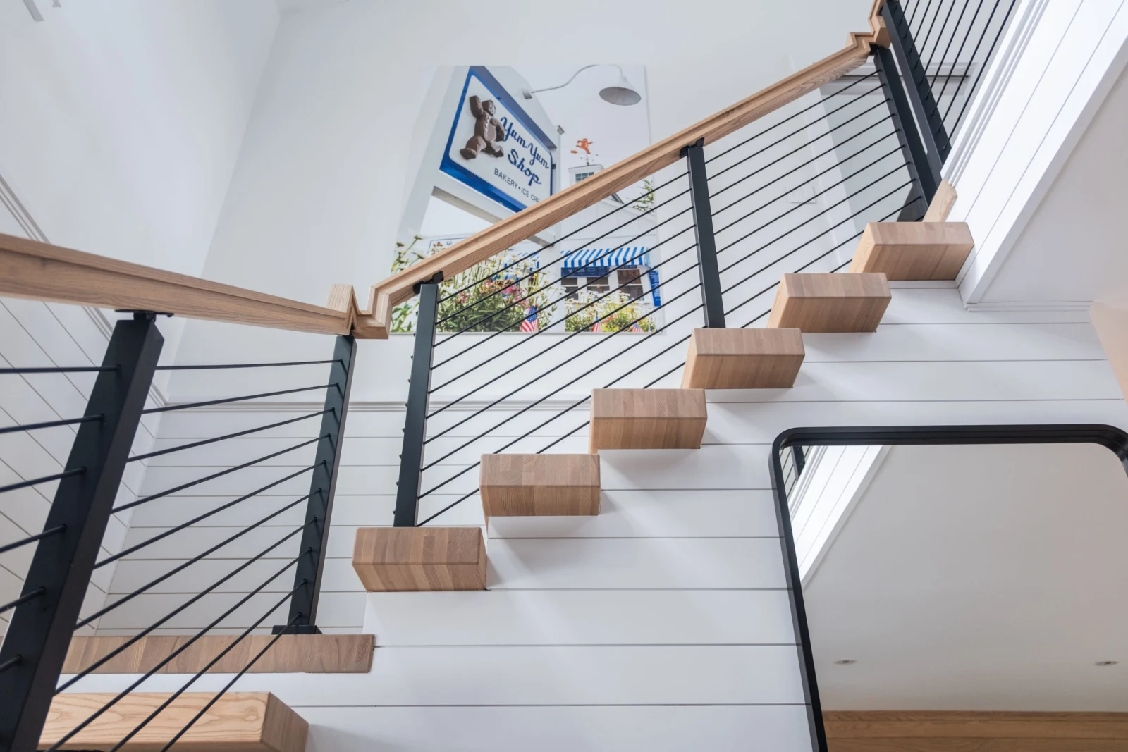 Upward view of treads cantilevered from white shiplap with black posts and cable infill