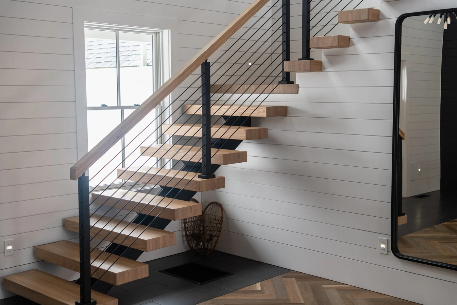Stair from the entry with rod railing climbing to the upper landing beside a mirror
